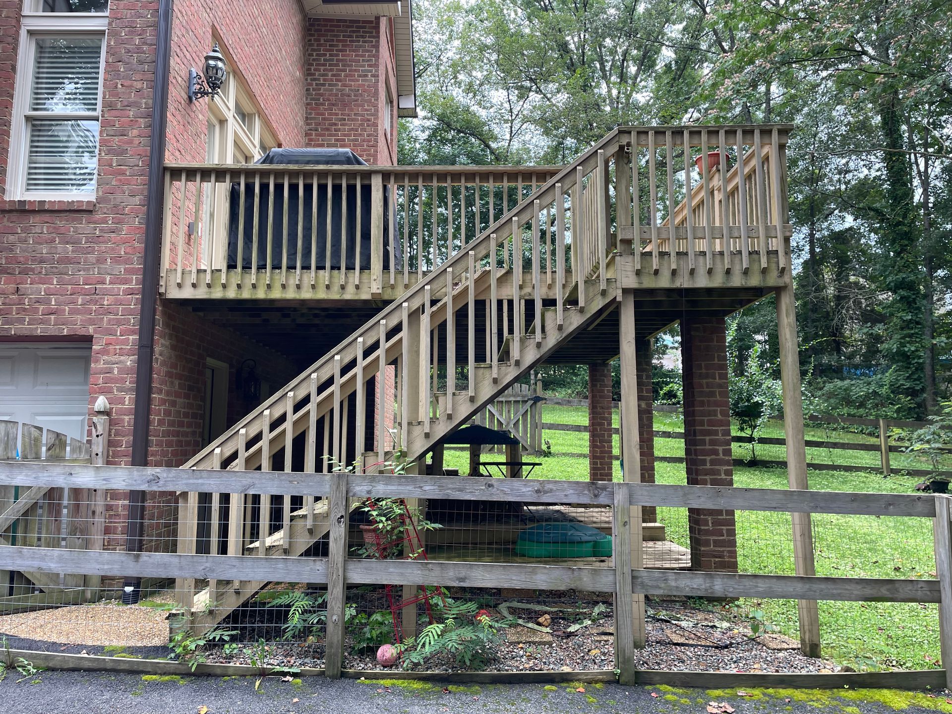 A wooden deck with stairs leading up to it is in front of a brick house.