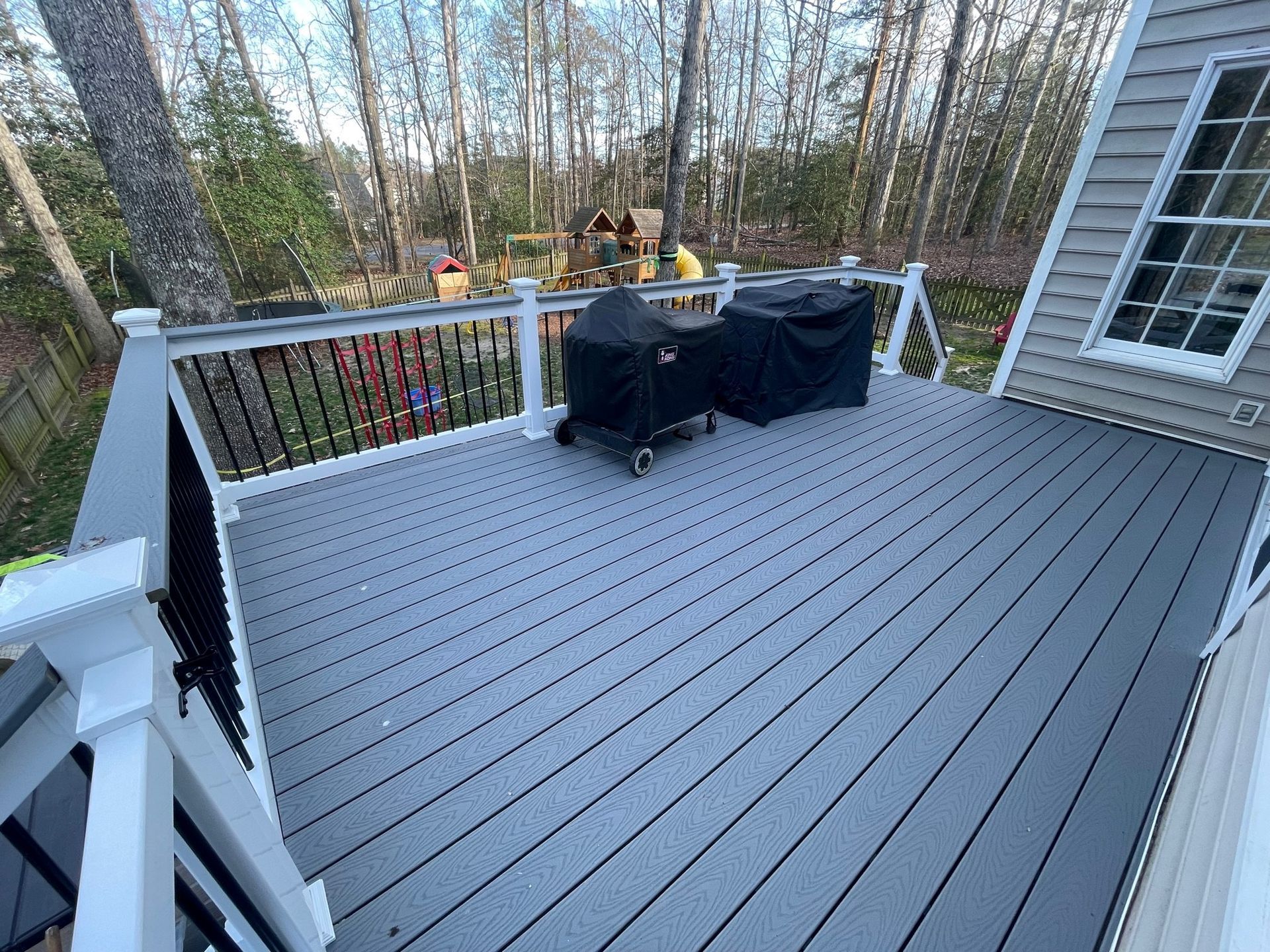 A gray deck with a white railing and a grill on it.