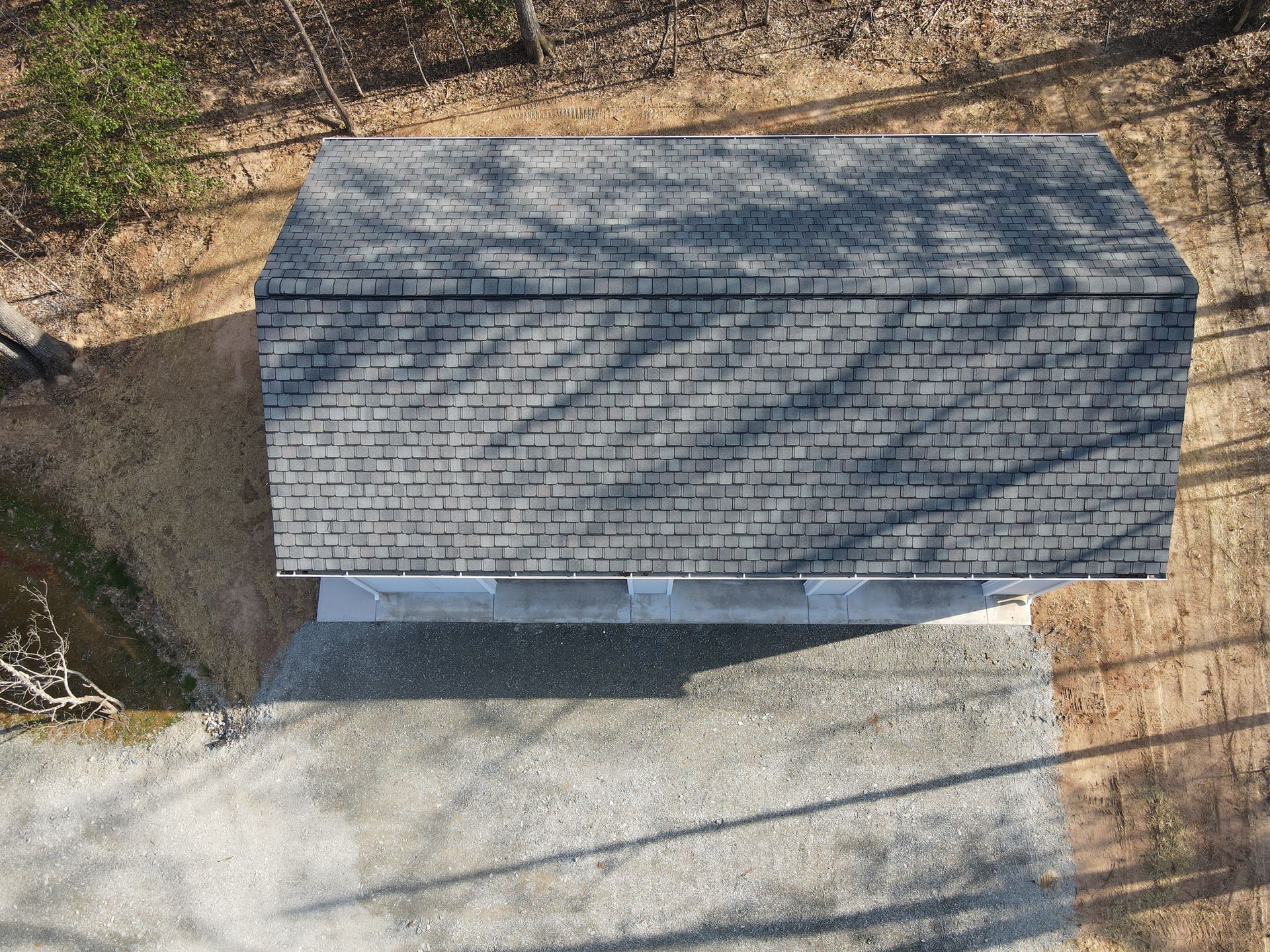 Overhead view of a shed with a gray shingled roof, set on a gravel driveway surrounded by trees.
