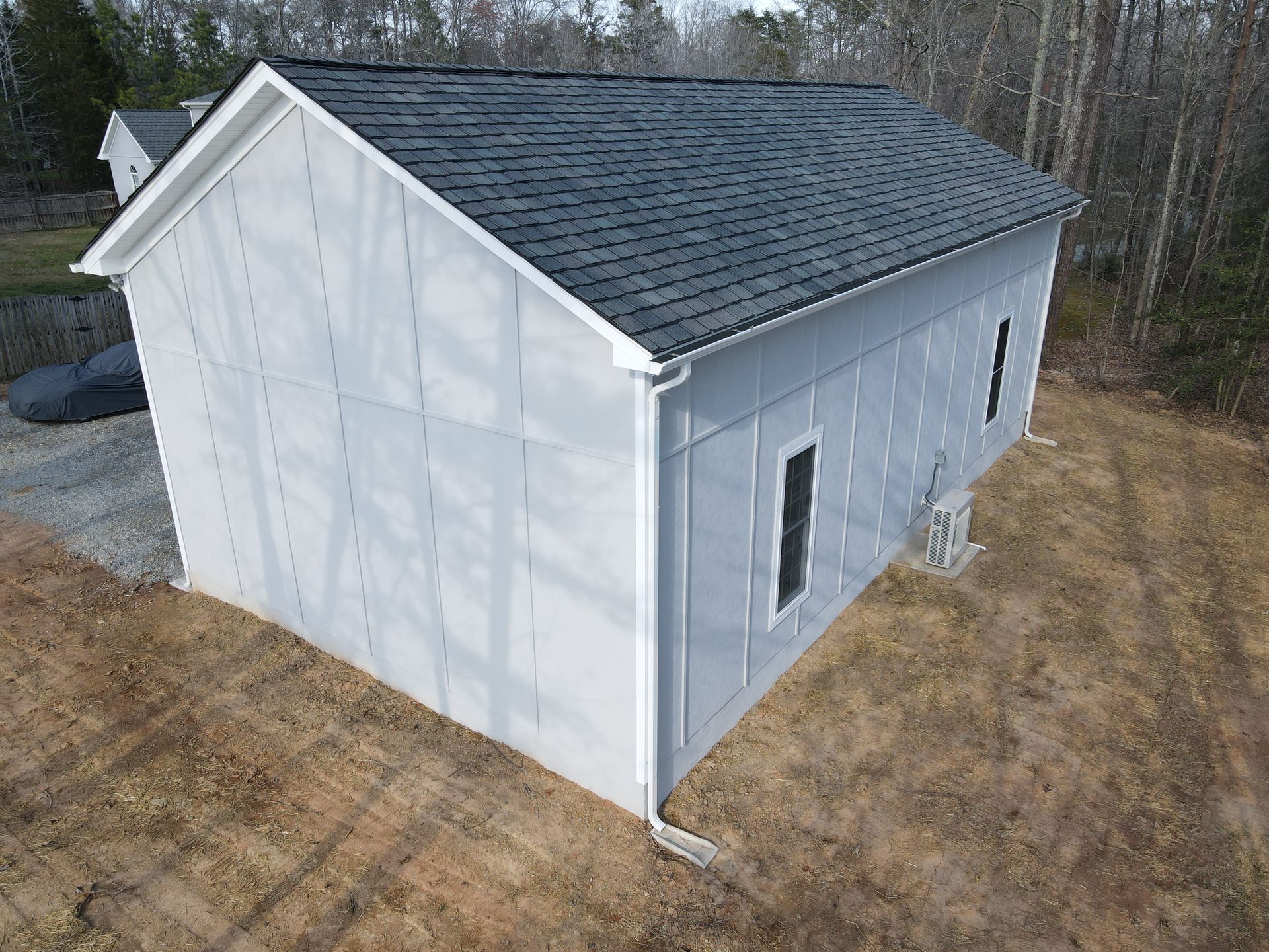 Gray building with dark roof in a wooded area.