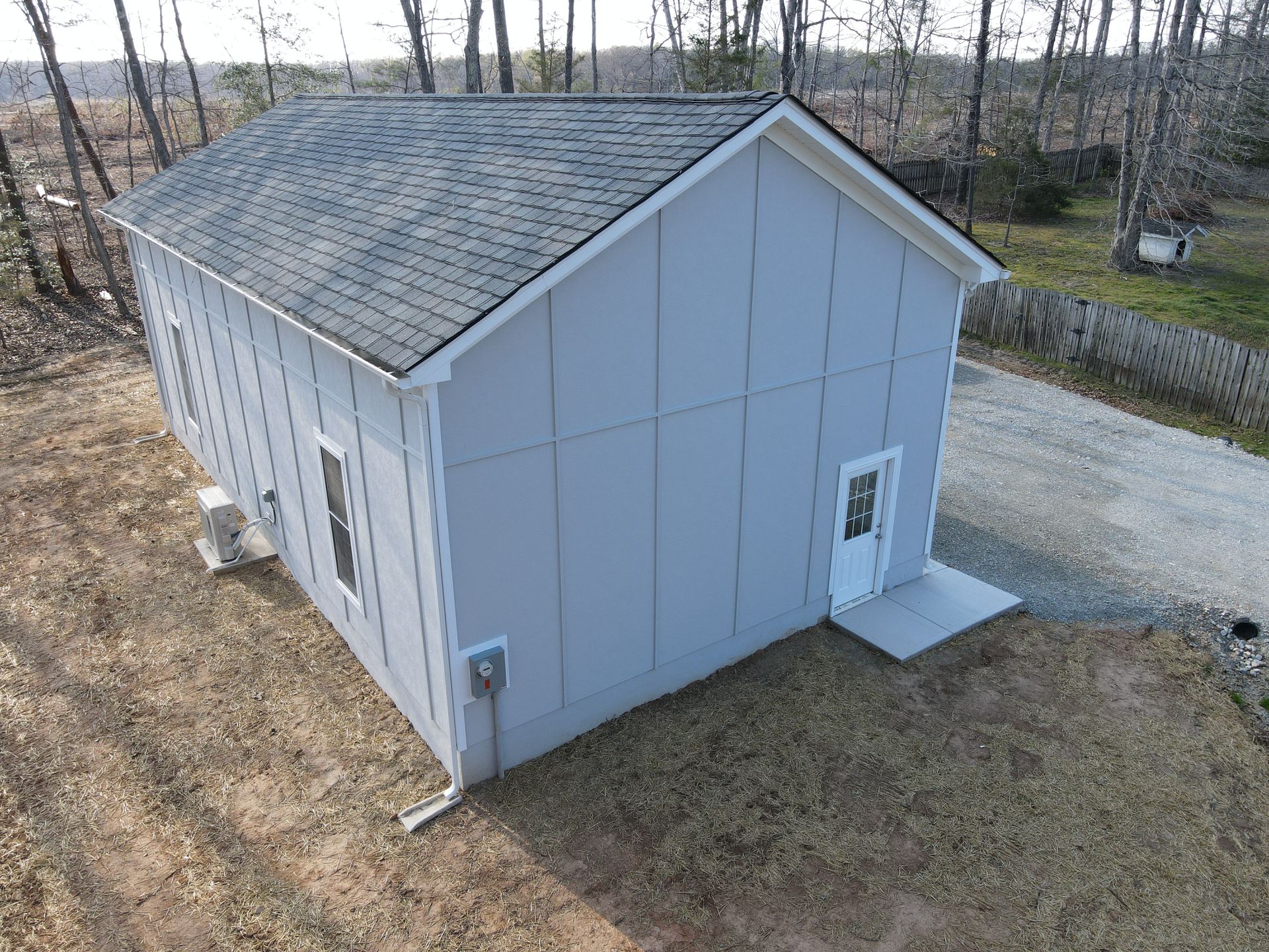 Gray, rectangular building with a dark roof and white trim, in a rural setting.