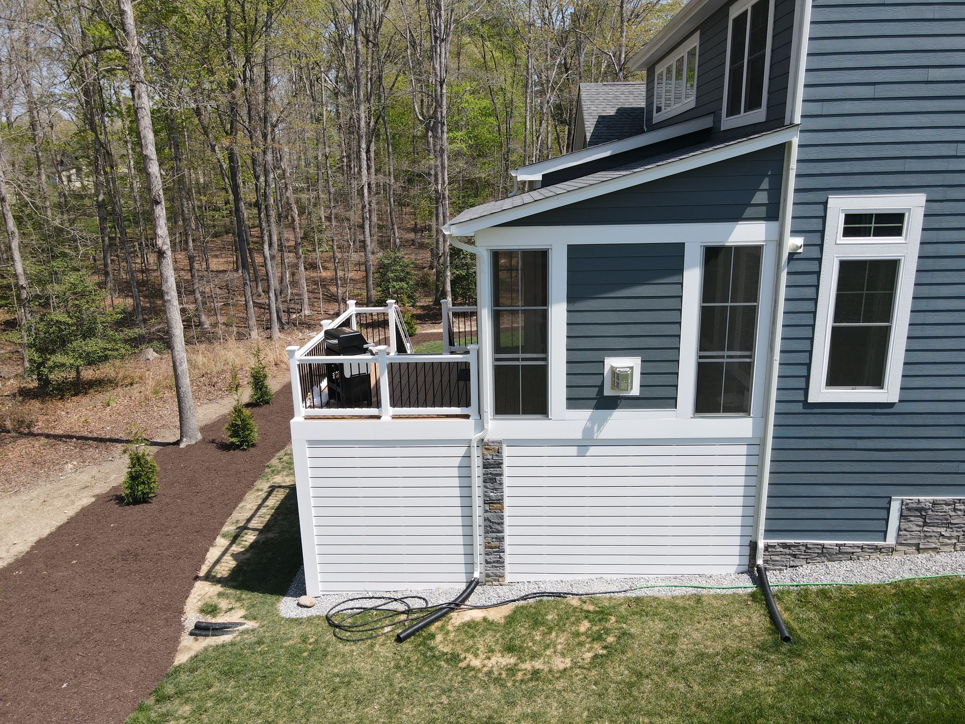 Side view of a blue-gray house with a white deck and surrounding trees.