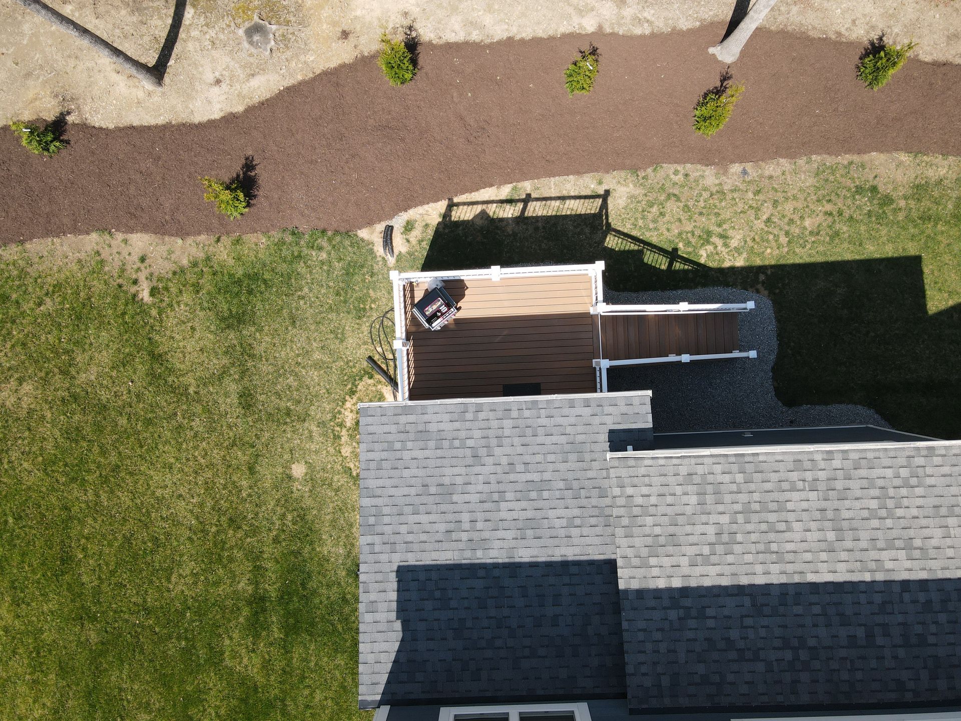 Aerial view of a house with a deck and landscaping; brown mulch, green grass.