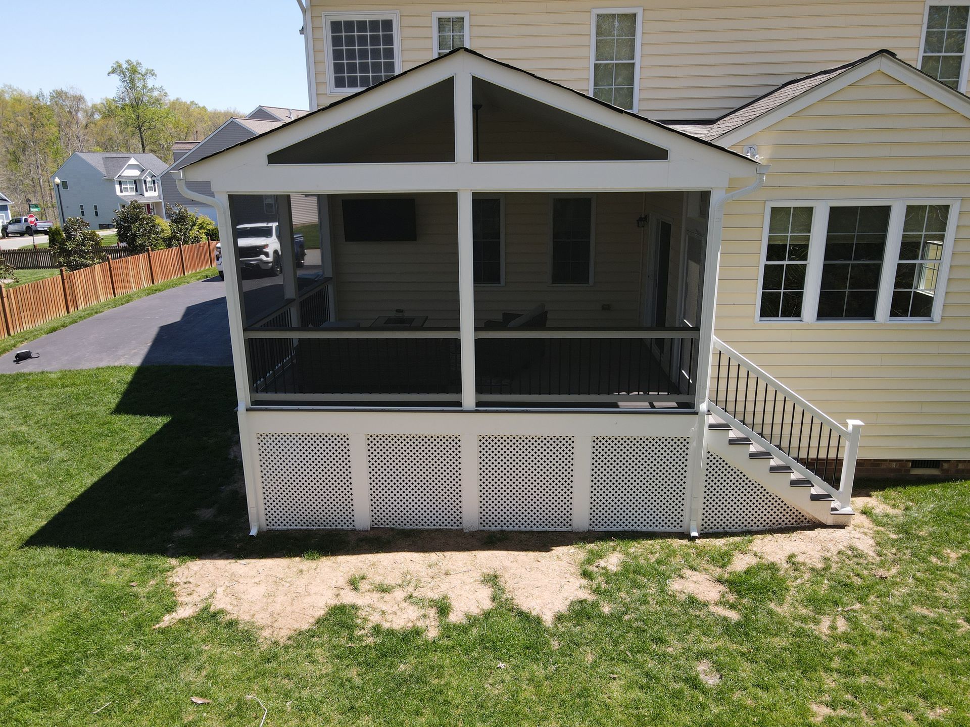 Screened porch attached to a yellow house with white trim. Stairs lead down to a grassy yard.