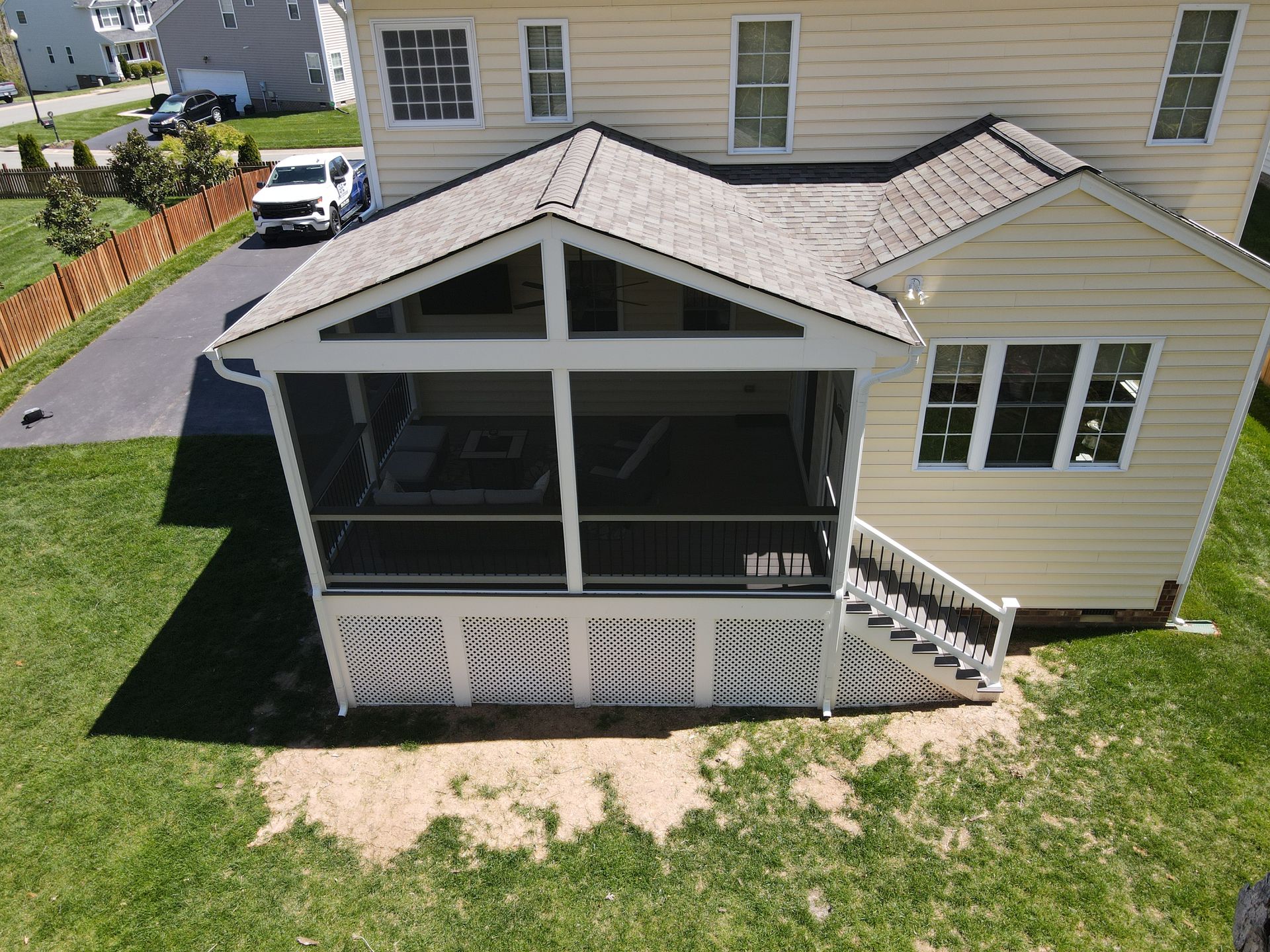 Screened-in porch attached to a two-story beige house with a driveway and green yard.