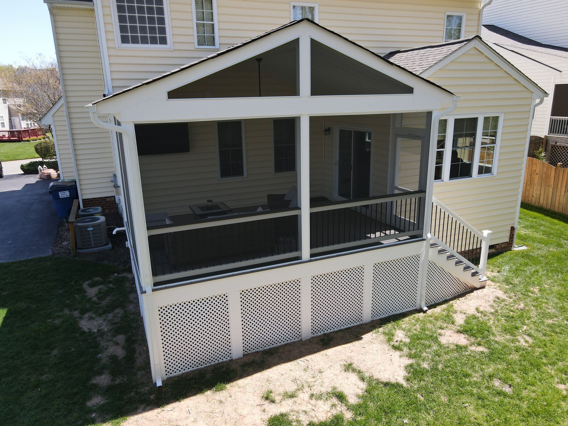 Screened-in porch attached to a yellow house, with white trim and lattice. Black railing. Green lawn.