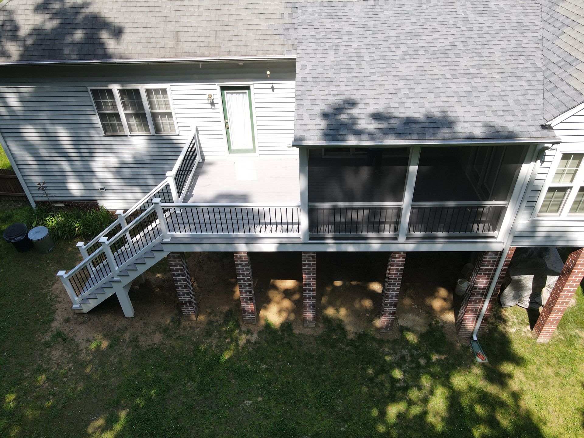 Overhead view of a house with a deck and screened porch on brick pillars. Green lawn surrounds the structure.