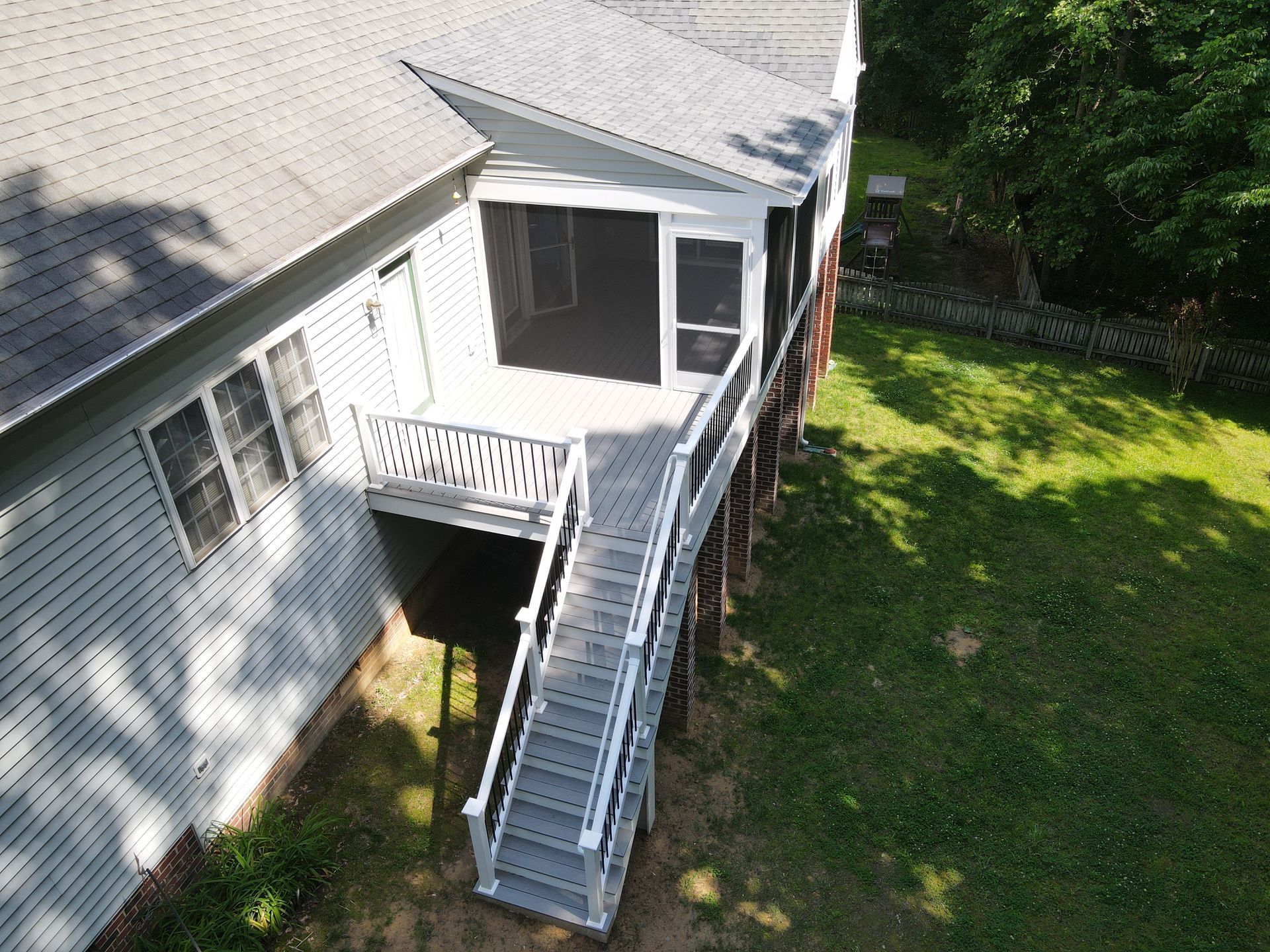 Exterior of a house with a gray deck and stairs leading to a screened porch, surrounded by green grass.