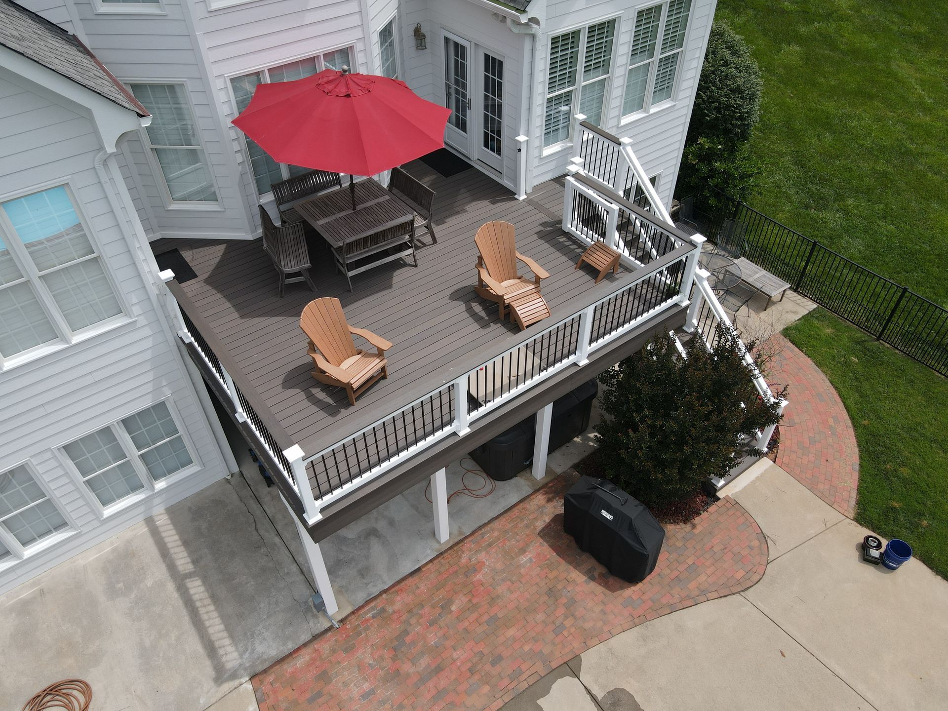 Elevated wooden deck with patio furniture, red umbrella, overlooking a yard, adjacent to a light-colored house.