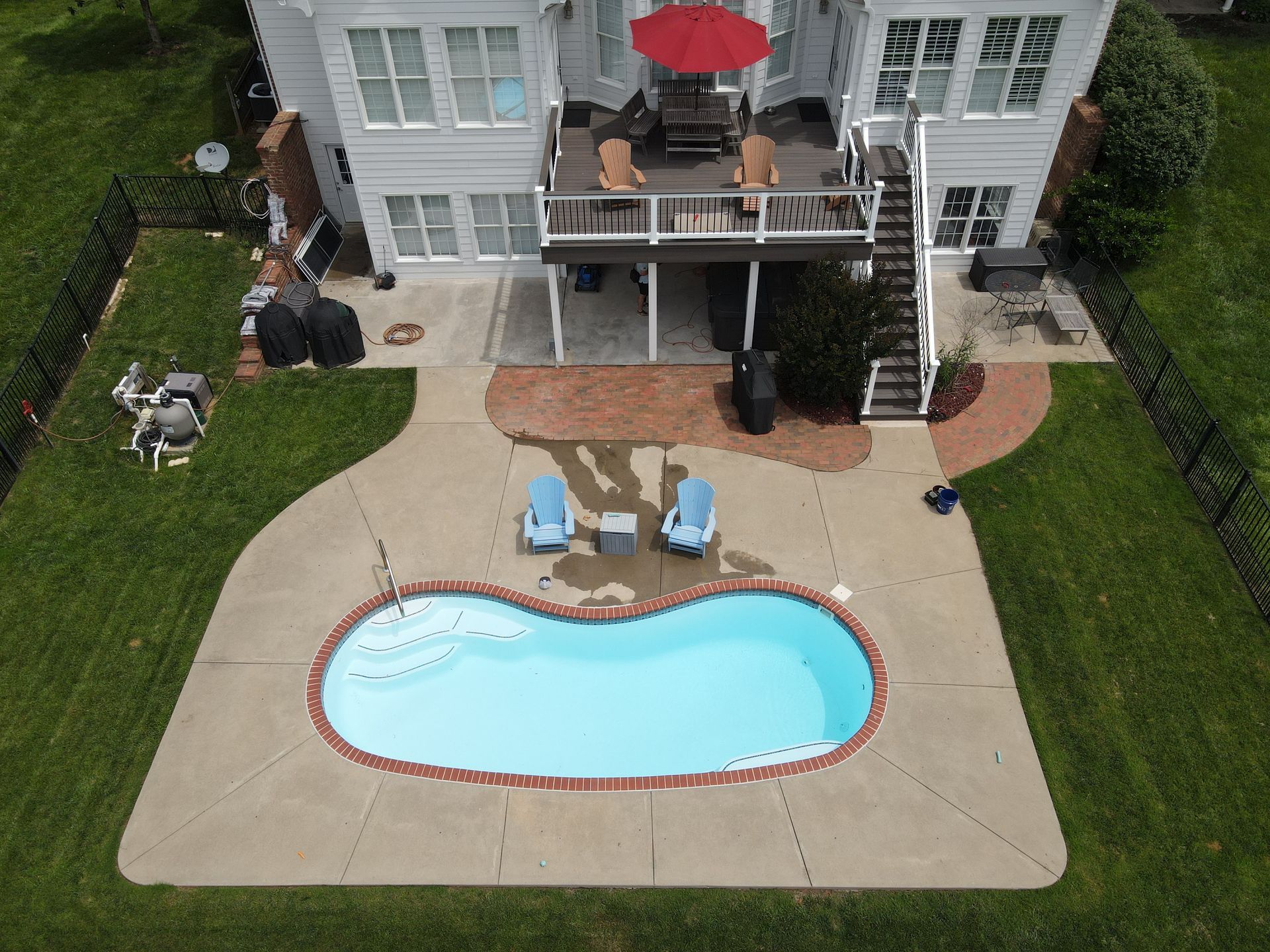 Aerial view of a white house with a pool, deck, and patio. Blue chairs surround the pool on the patio.