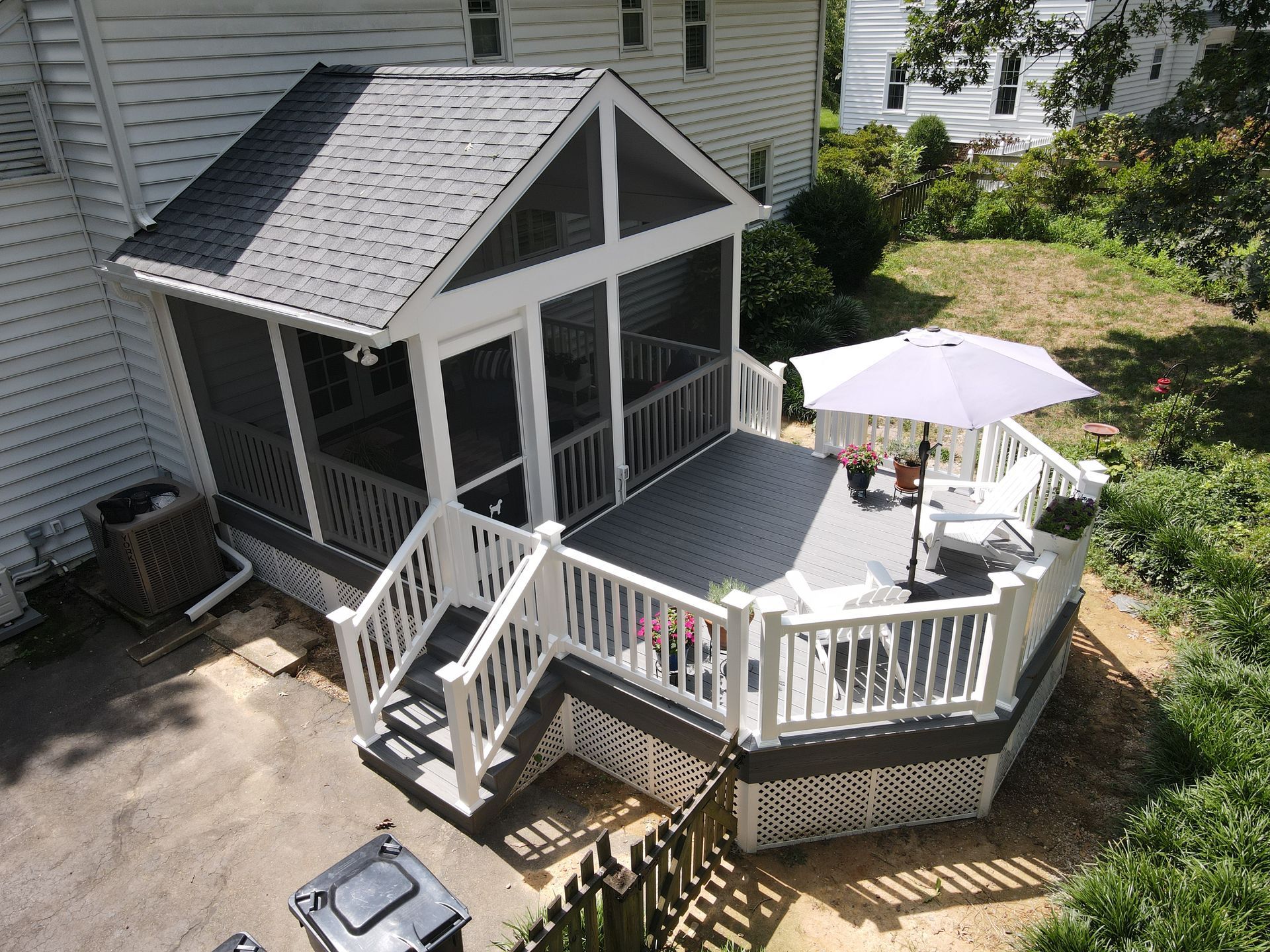 Screened-in porch and deck attached to a house with a gray roof, white railings, and a gray deck.