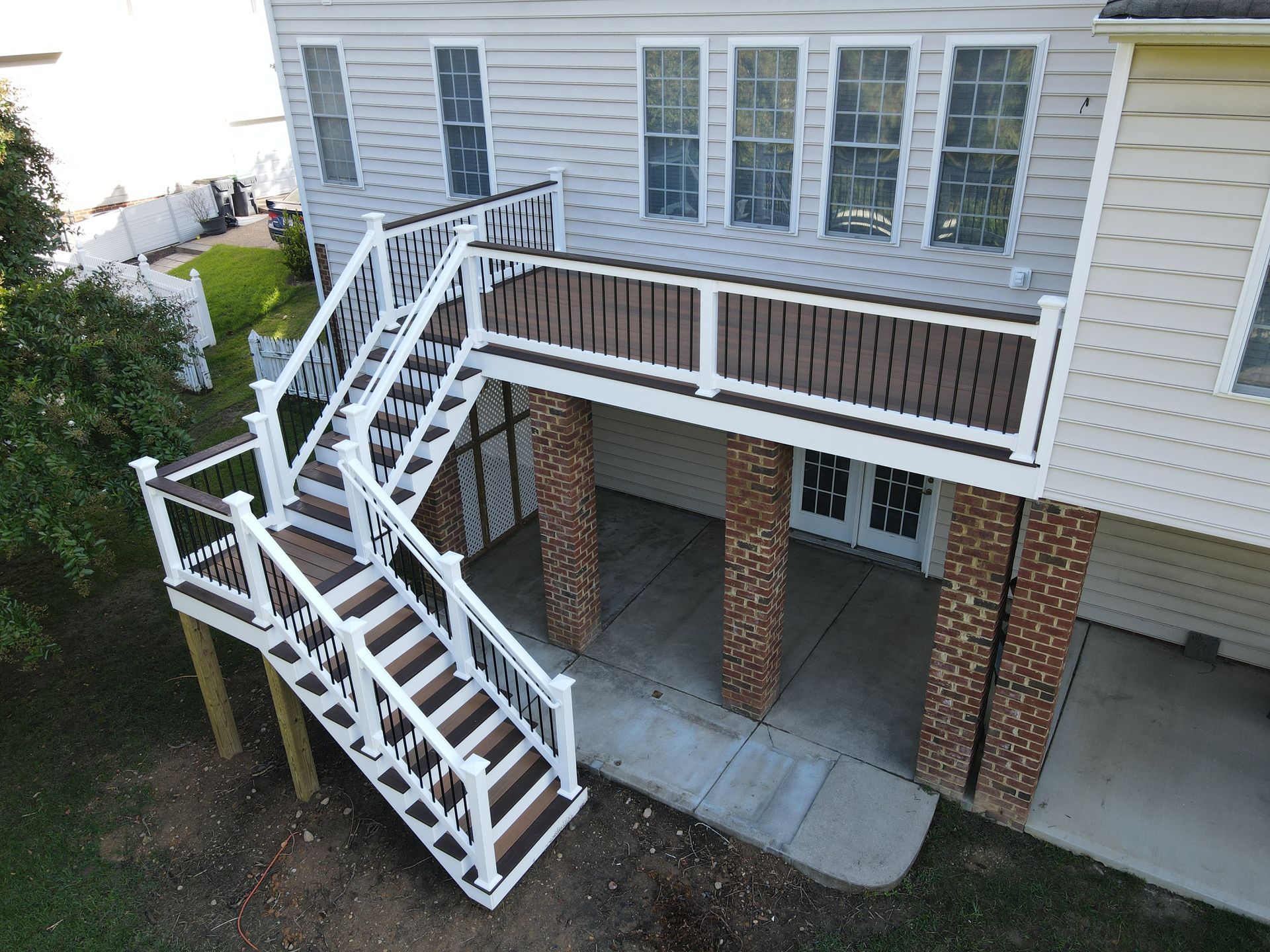 A two-story deck with stairs, brown and white railings, and brick columns.