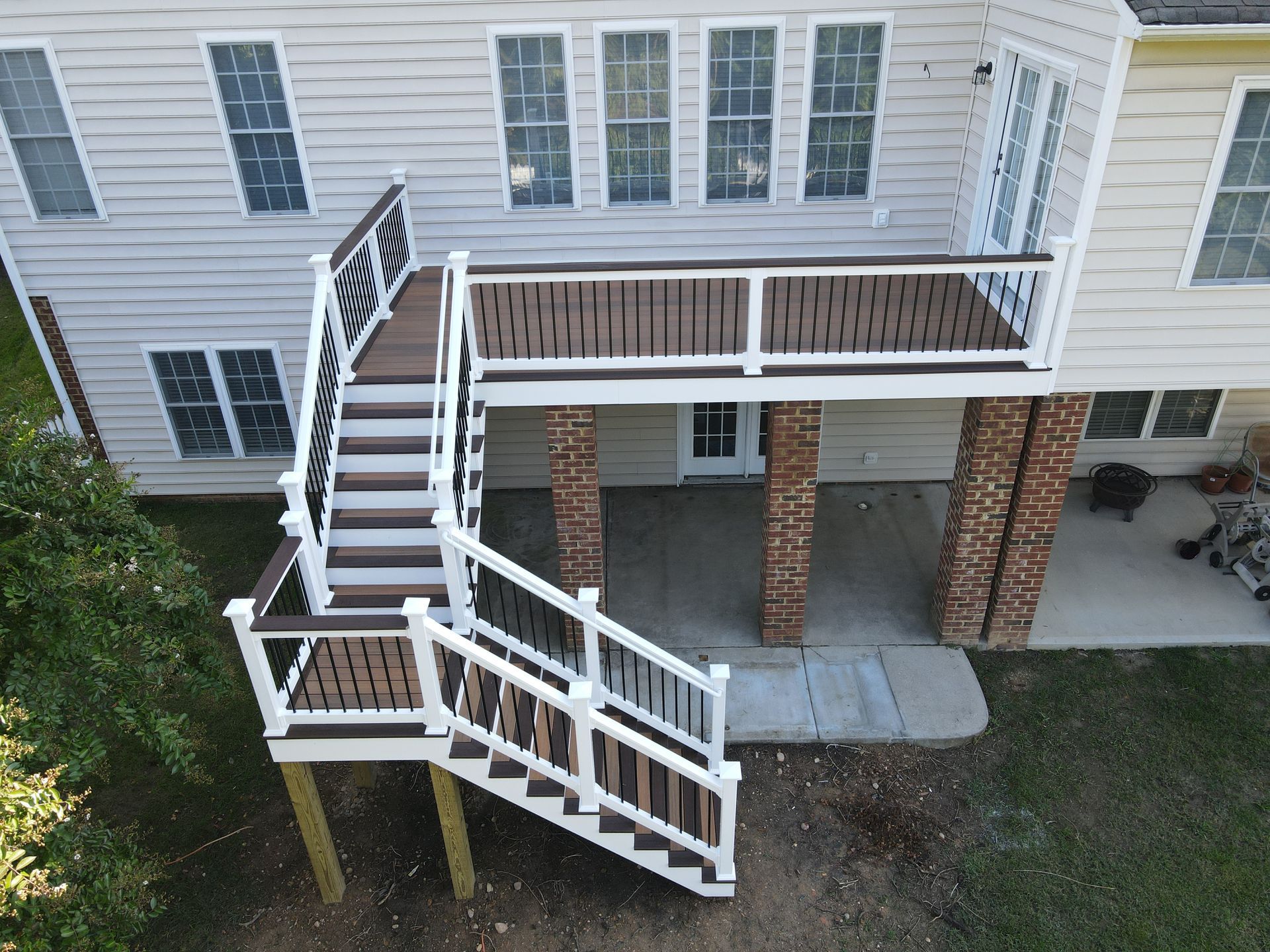 Two-story house with a wooden deck, stairs, and brick columns. Brown and white color scheme.