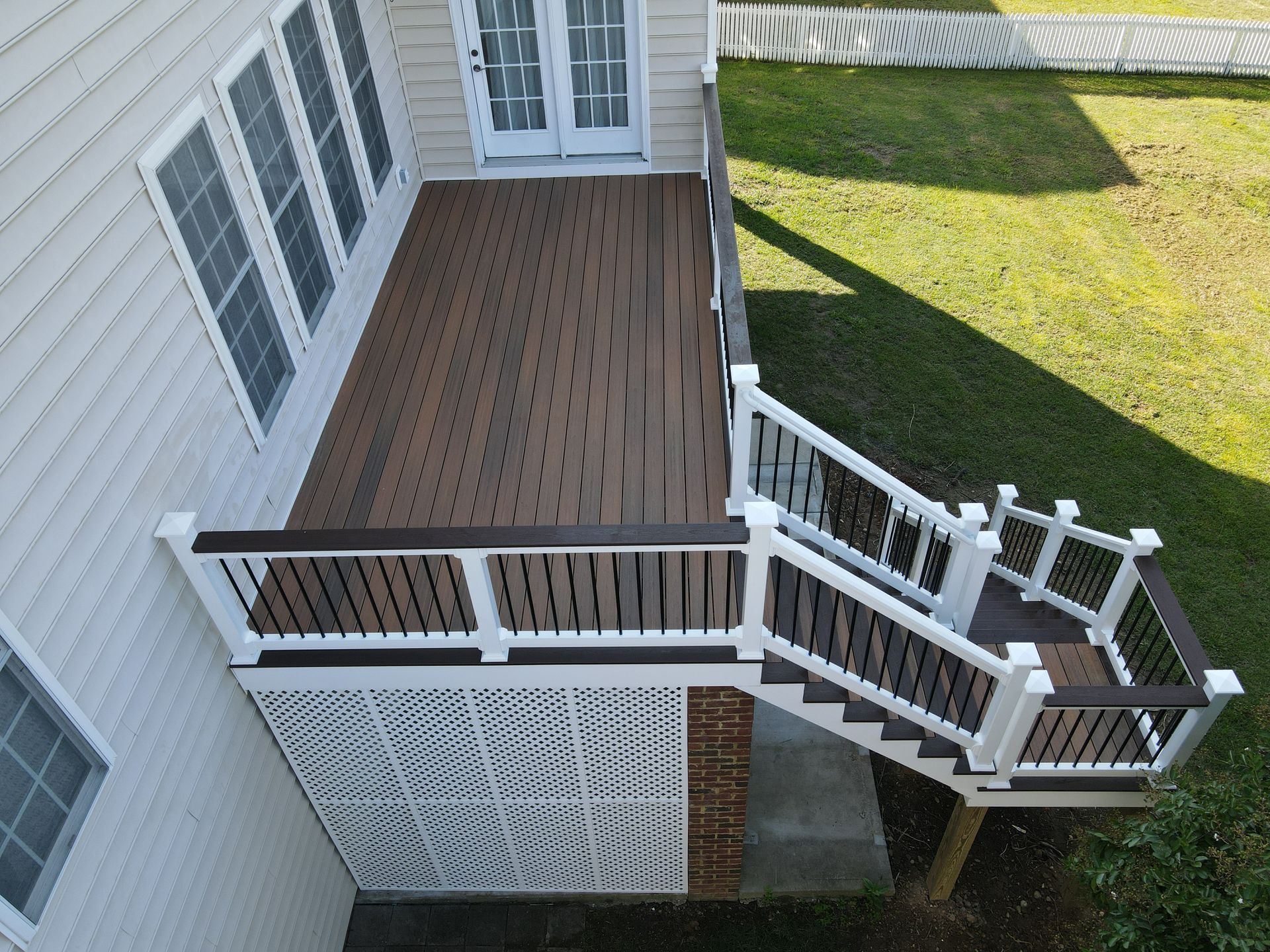 A brown and white deck attached to a house with steps leading to a yard with green grass.
