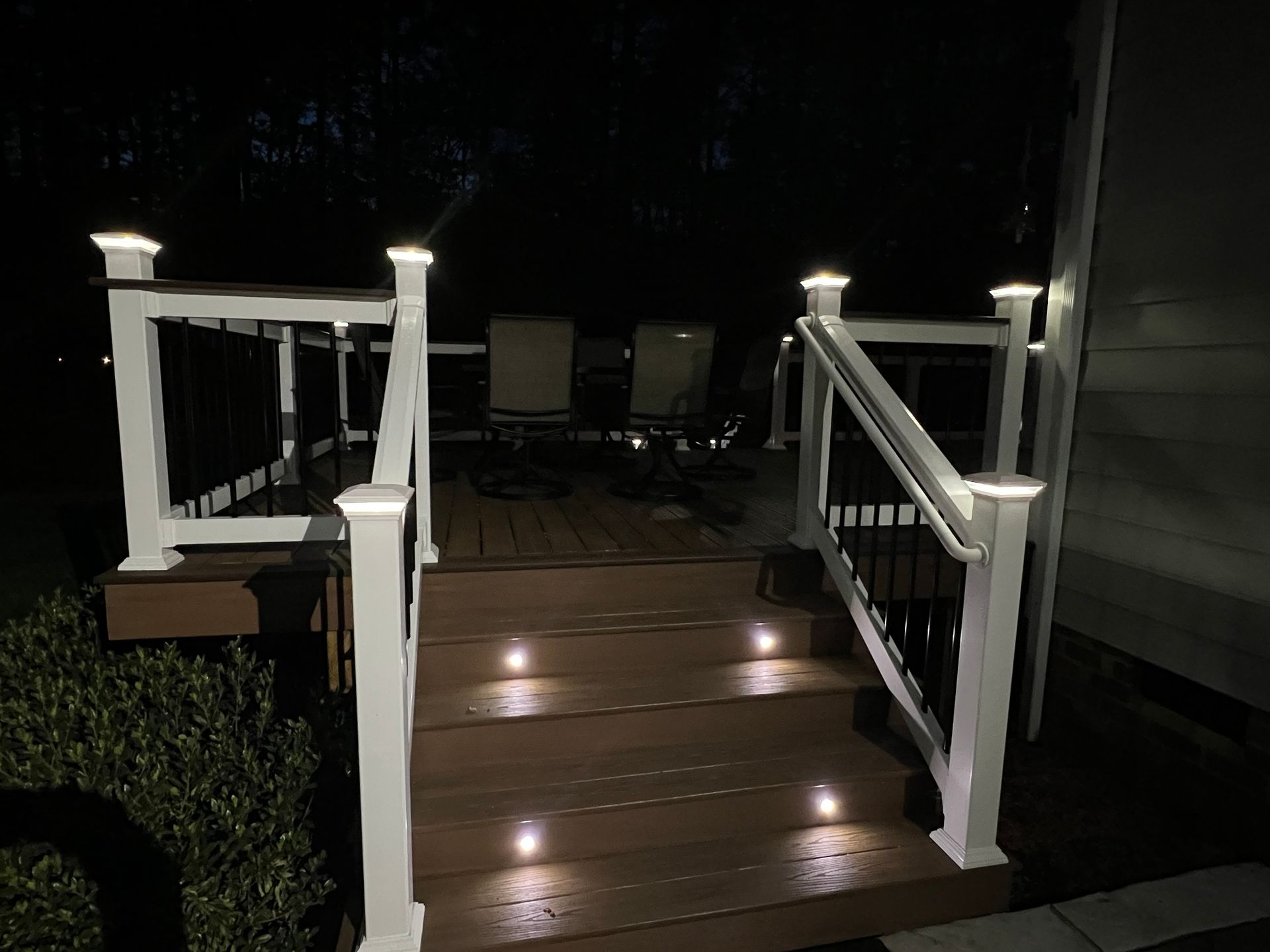 A deck with stairs and railing is lit up at night.