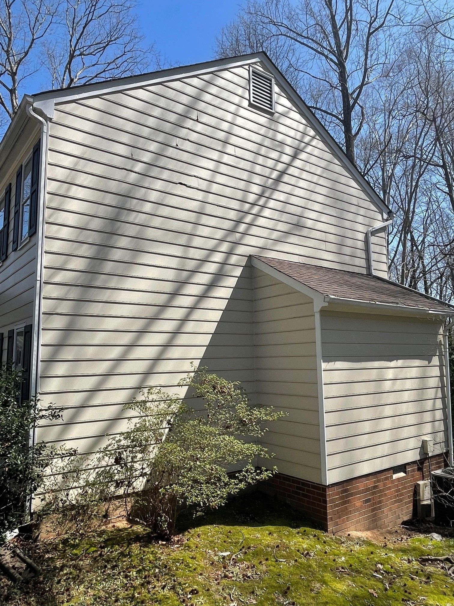 The side of a house with a garage and trees in the background.