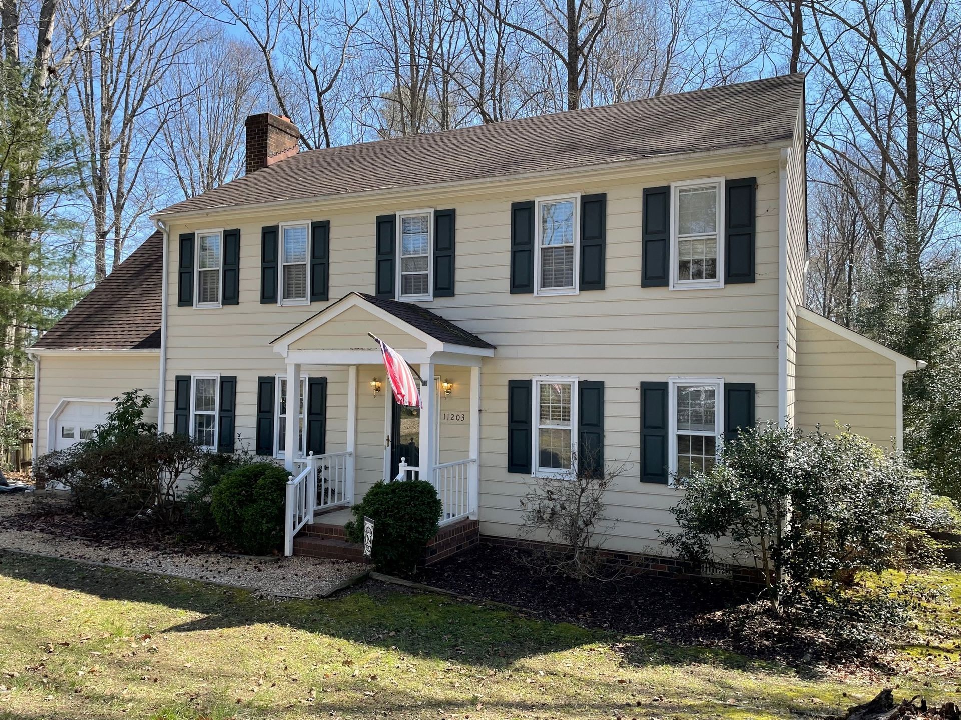 A large white house with black shutters and a red flag on the front porch.