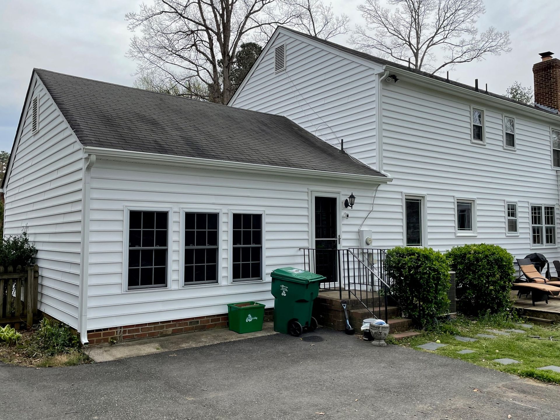 A white house with a green trash can in front of it.