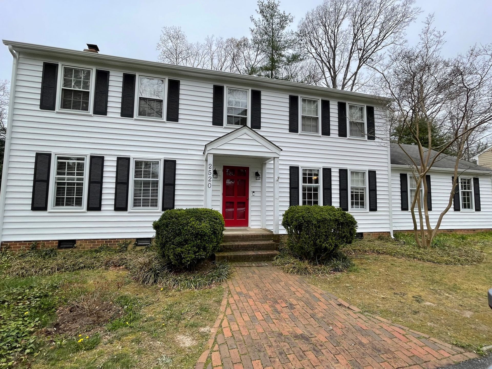 A white house with black shutters and a red door.