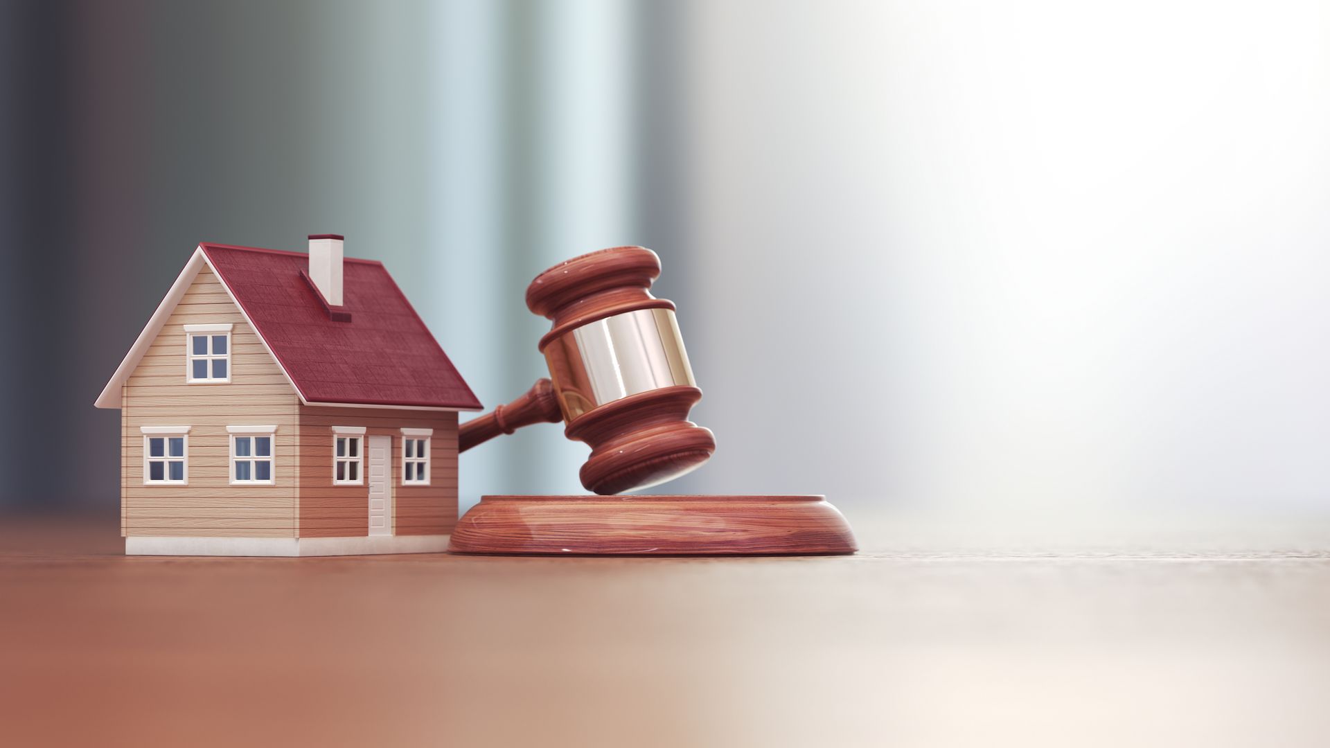 A wooden gavel is sitting next to a model house on a wooden table.