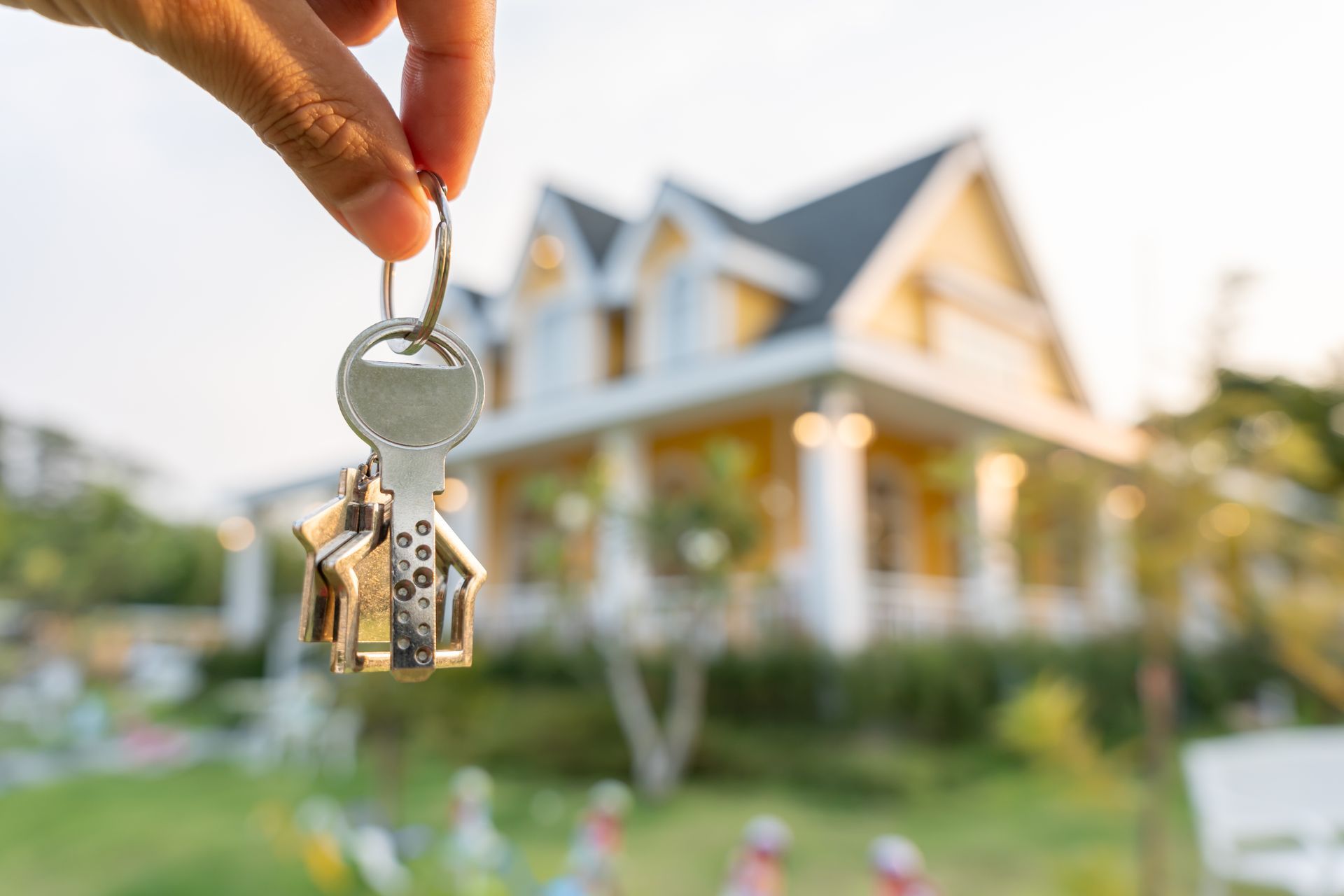 A person is holding a pair of keys in front of a house.