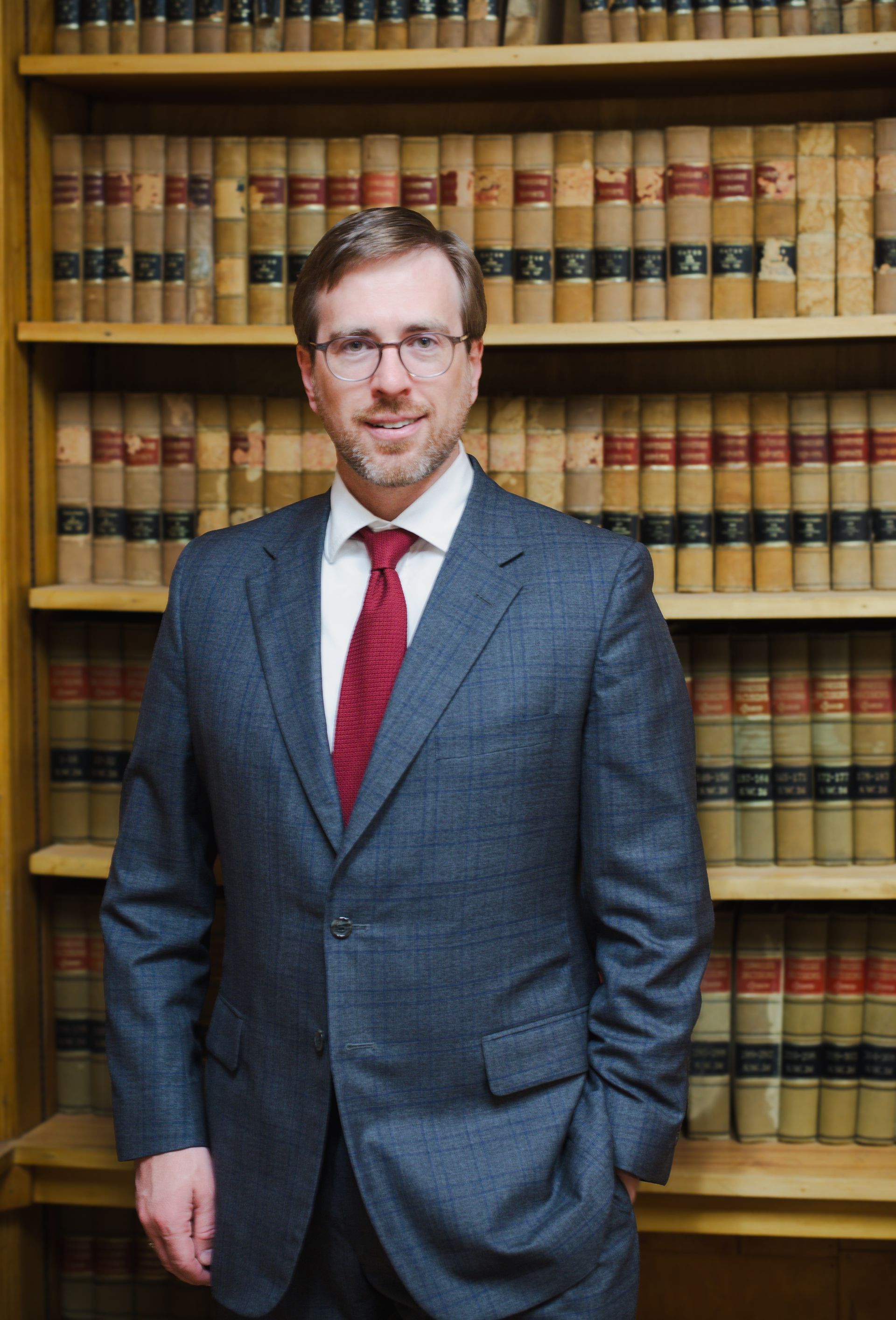 Attorney Sheridan Randolph in a suit and tie is standing in front of a bookshelf filled with books.