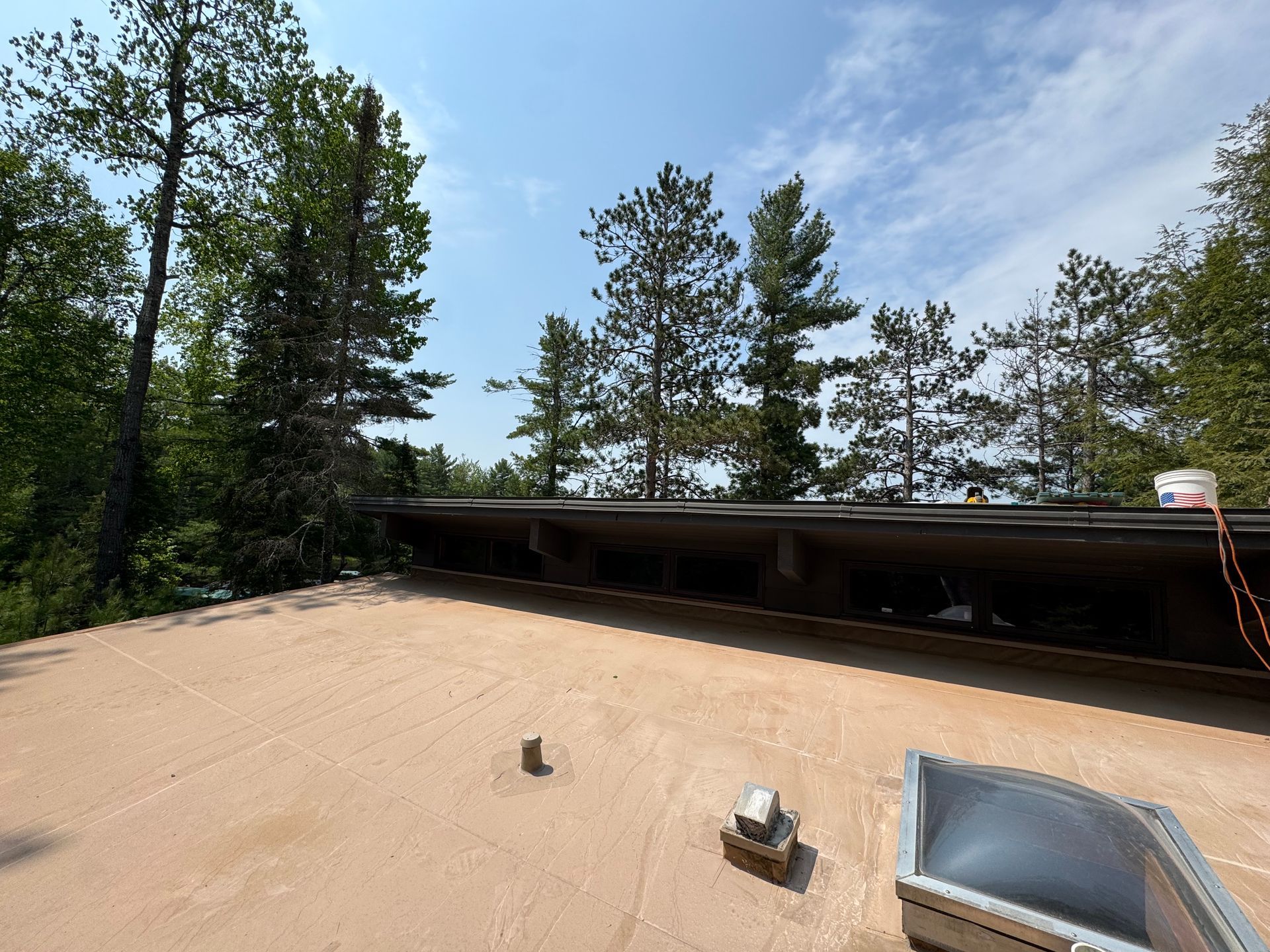 Flat roof with trees and blue sky. A light-colored surface with a small object and equipment.