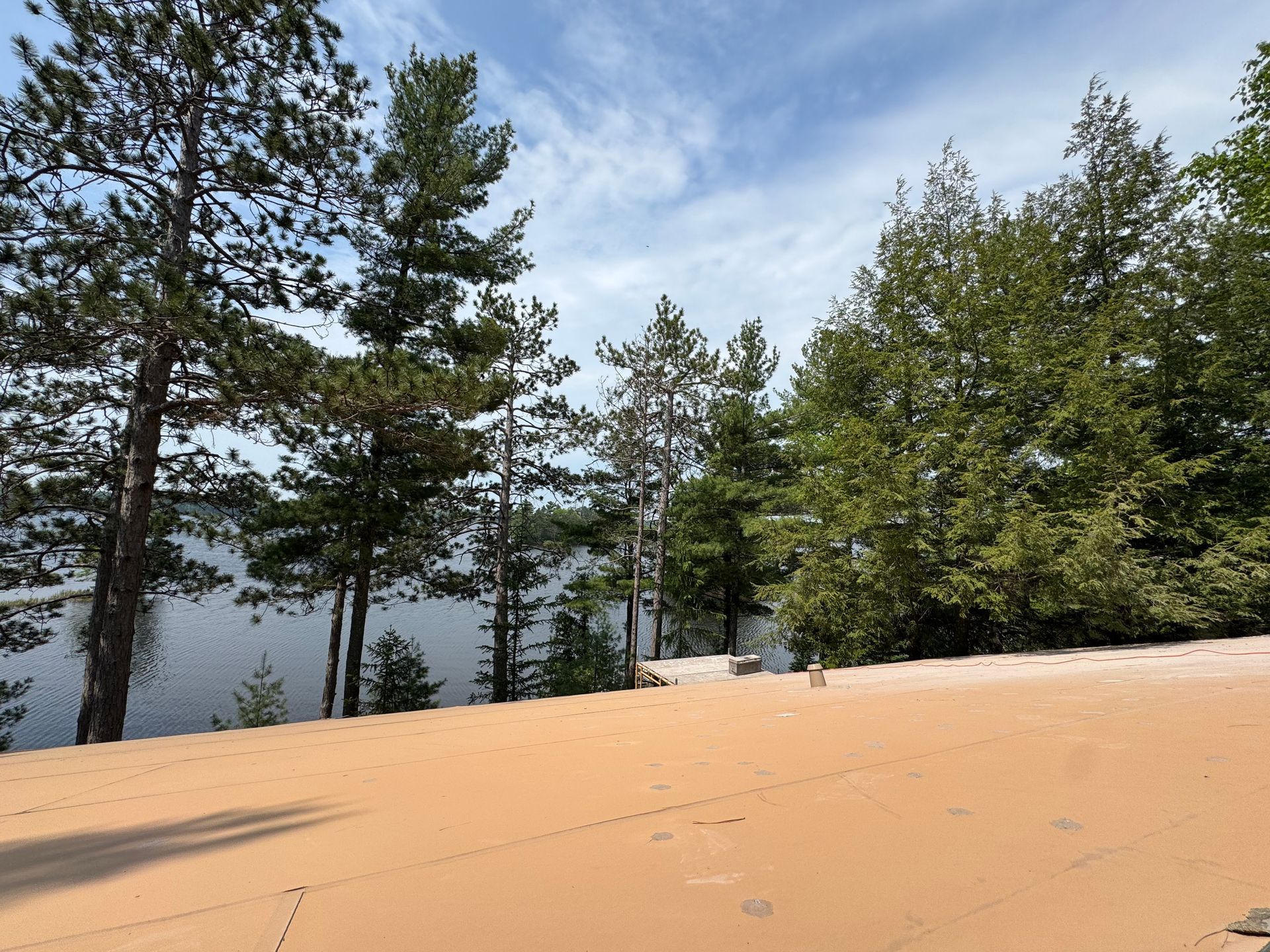 Brown deck overlooking a lake, surrounded by green trees under a cloudy sky.