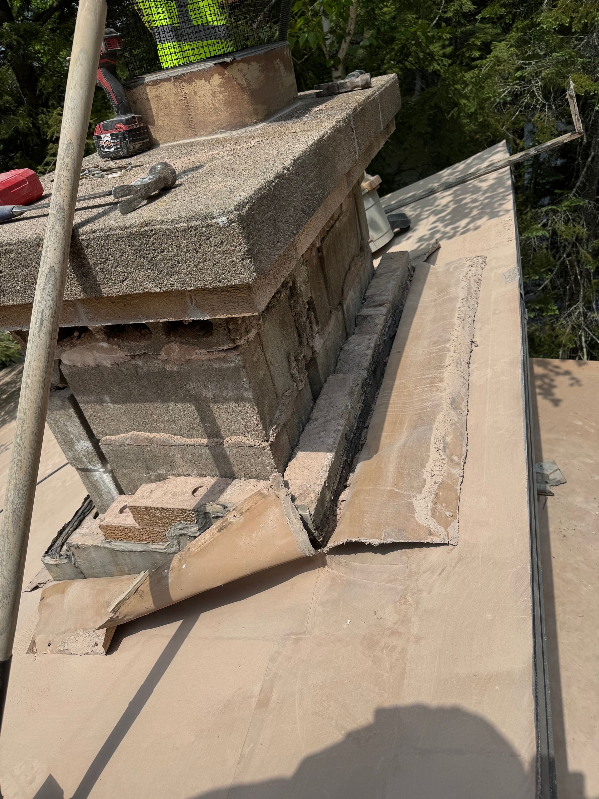 Rooftop view of a chimney with crumbling bricks, showing damage and repair progress.