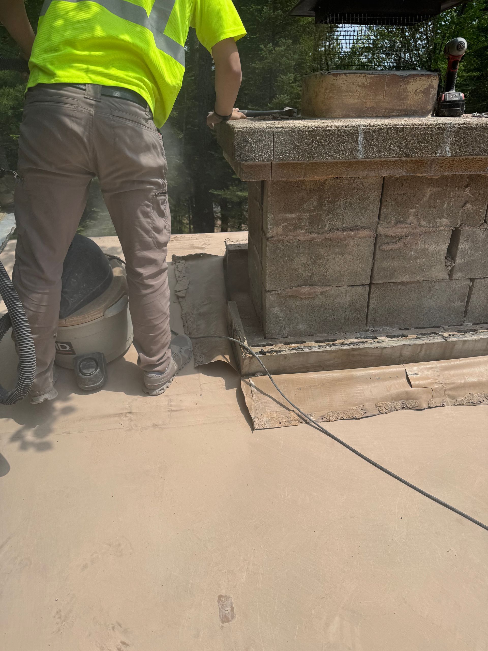 Construction worker in safety vest cutting concrete block structure with a saw on a sandy surface.