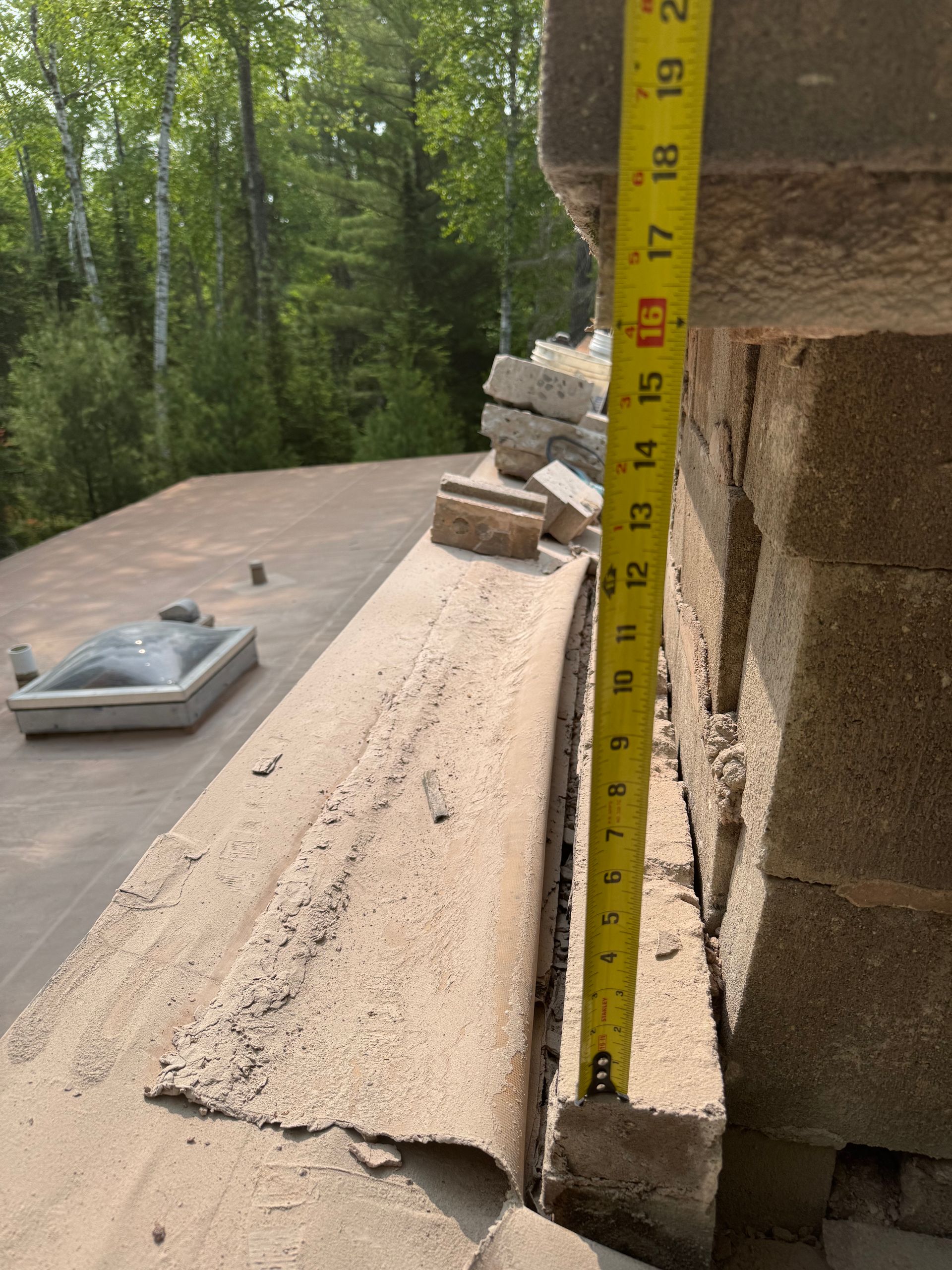 A tape measure shows a 17-inch gap between a roof's edge and a brick chimney.