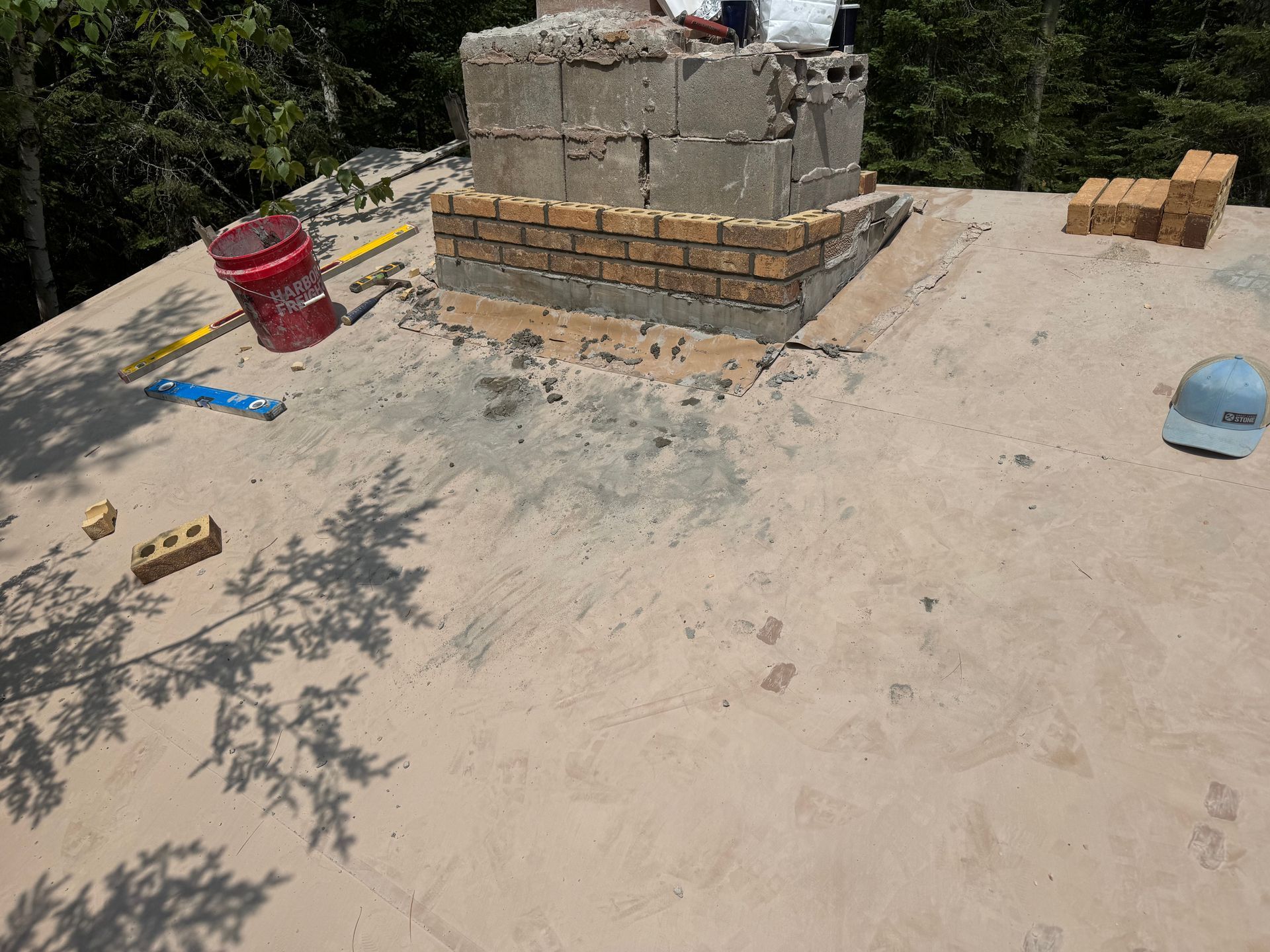 Chimney being constructed on a rooftop, with bricks, blocks, and tools scattered nearby.