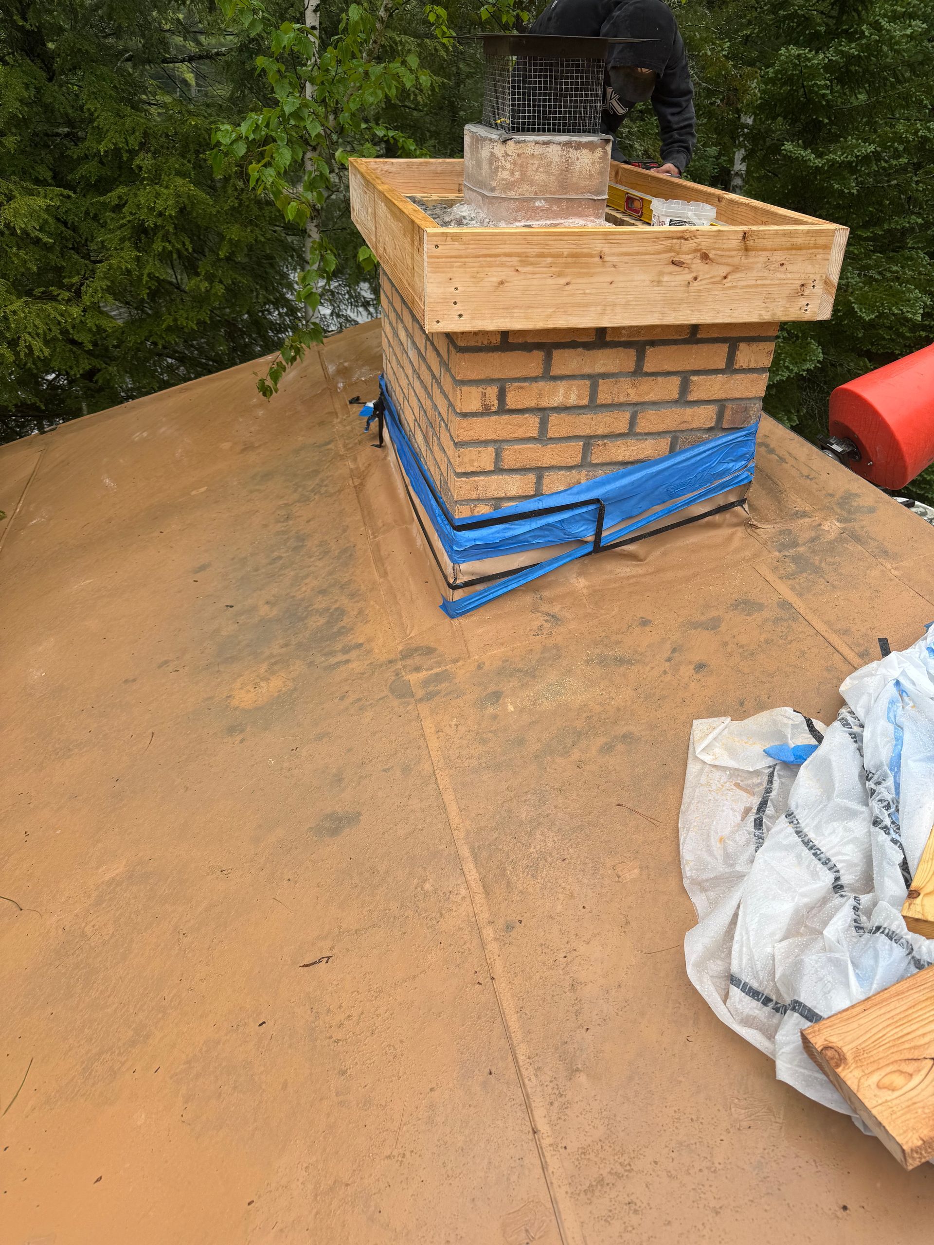 Chimney under construction on a brown roof; a person works at the top.