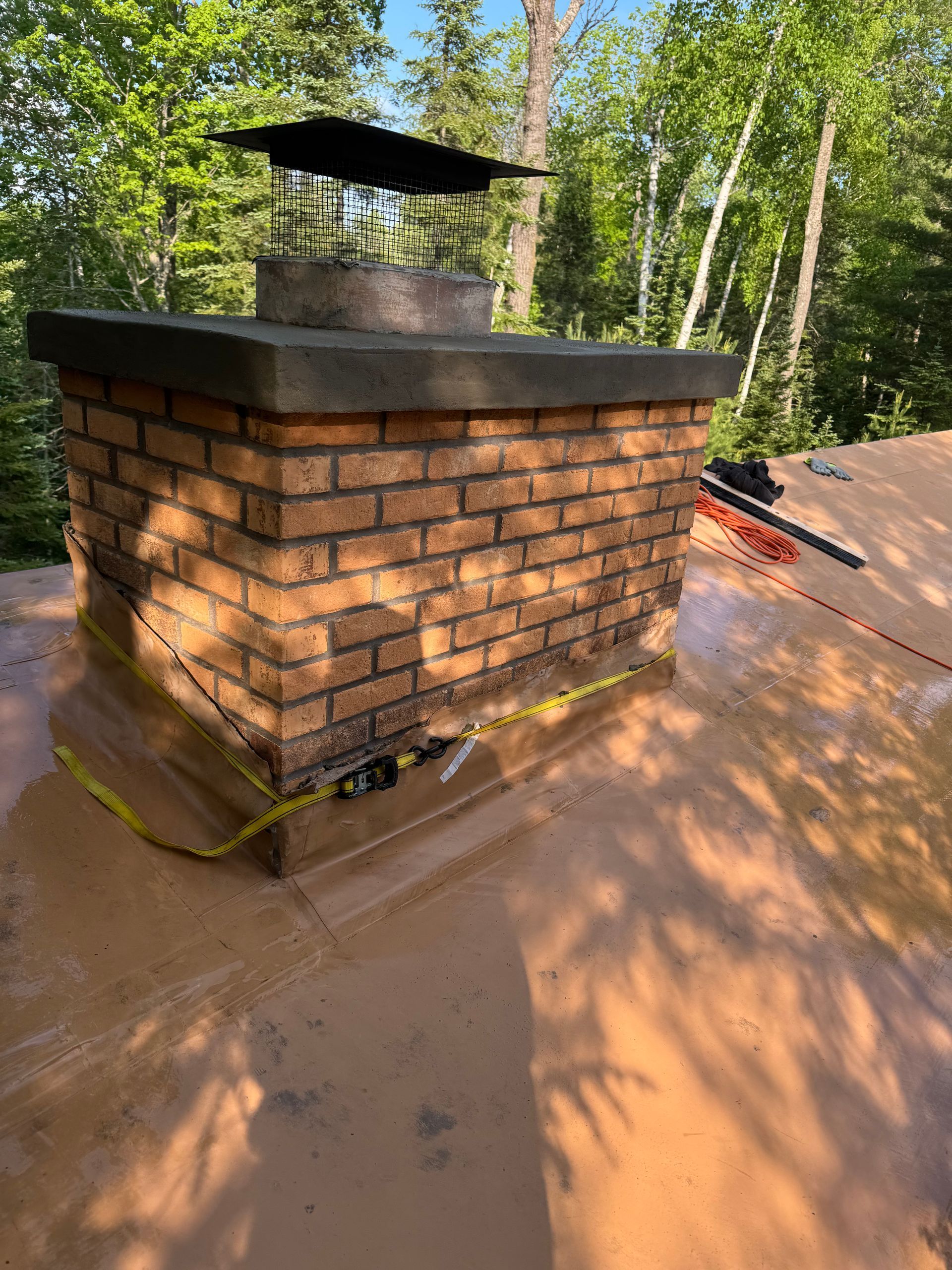 Brick chimney on a brown roof, surrounded by trees. Yellow caution tape is present.
