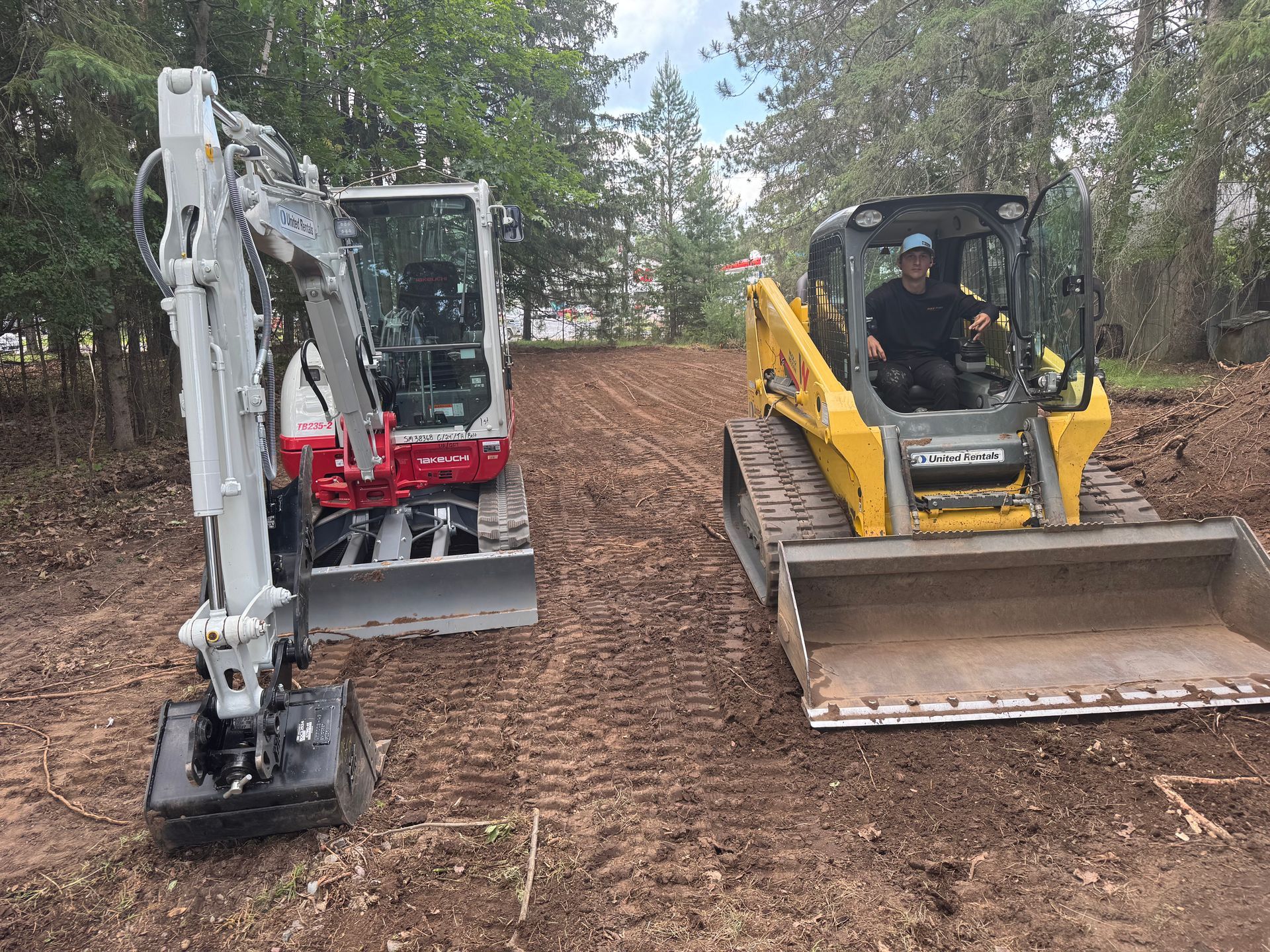 Mini excavator and skid steer on dirt, grading the terrain. A person drives the skid steer.