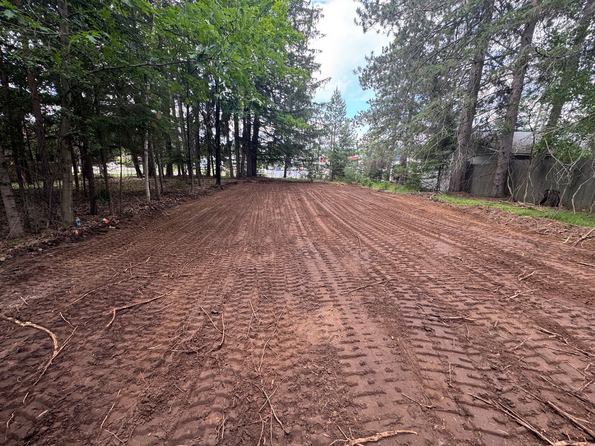 Brown dirt clearing with tire tracks, surrounded by trees under a cloudy sky.