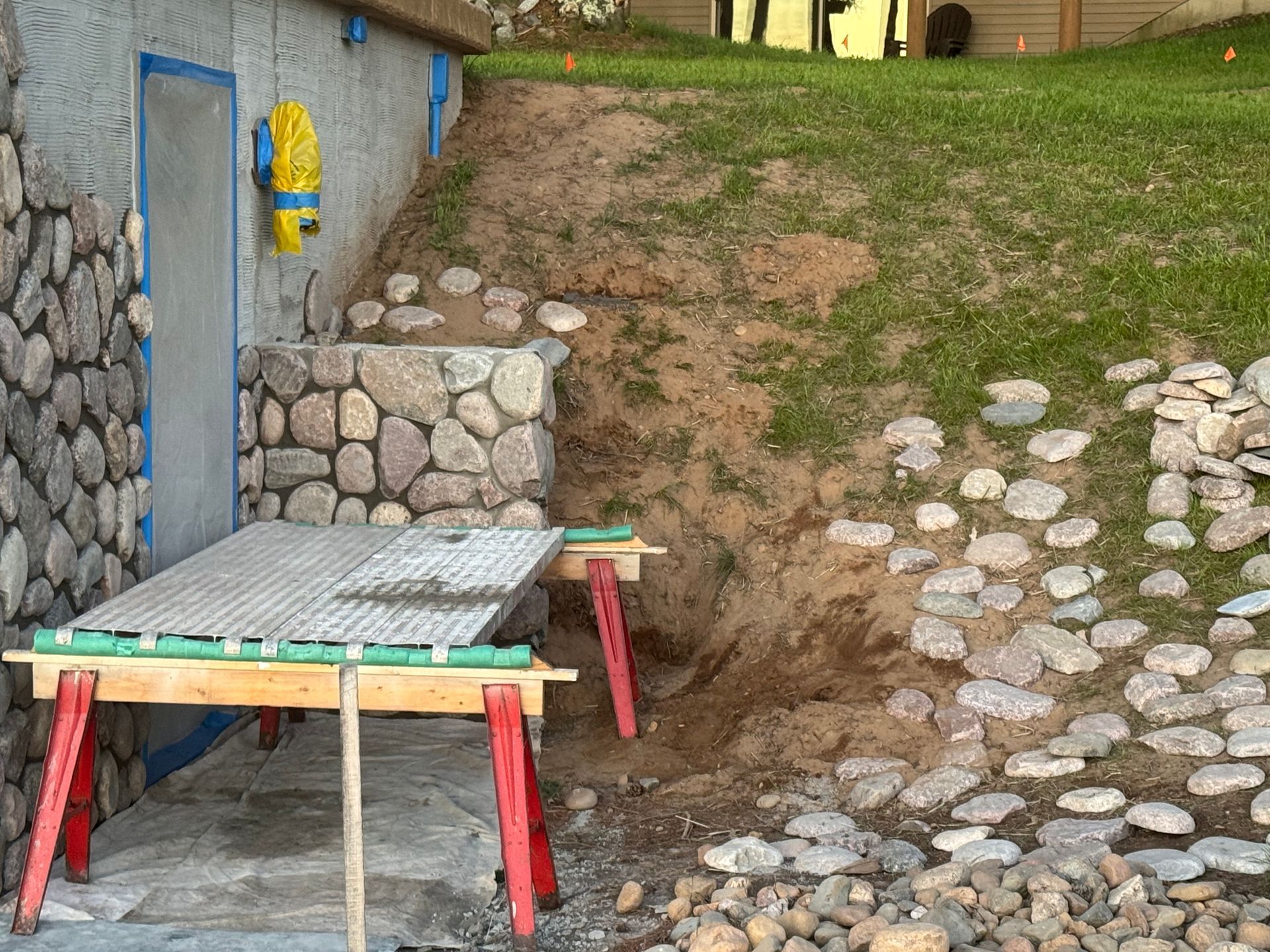 Construction site with stonework, dirt, grass, and a table supported by sawhorses.
