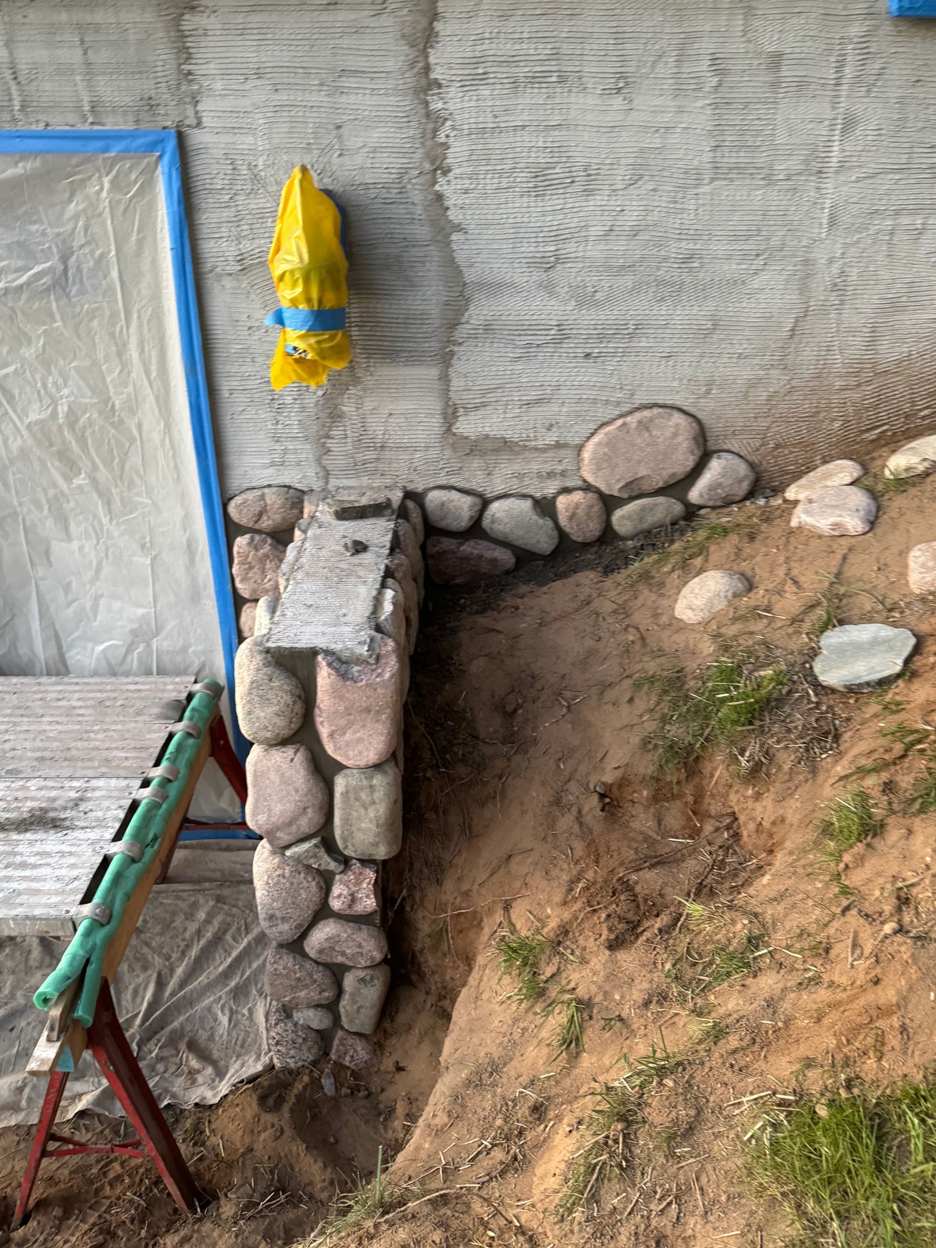 Stone pillar with water feature and yellow plastic duck, next to a sandy bank.