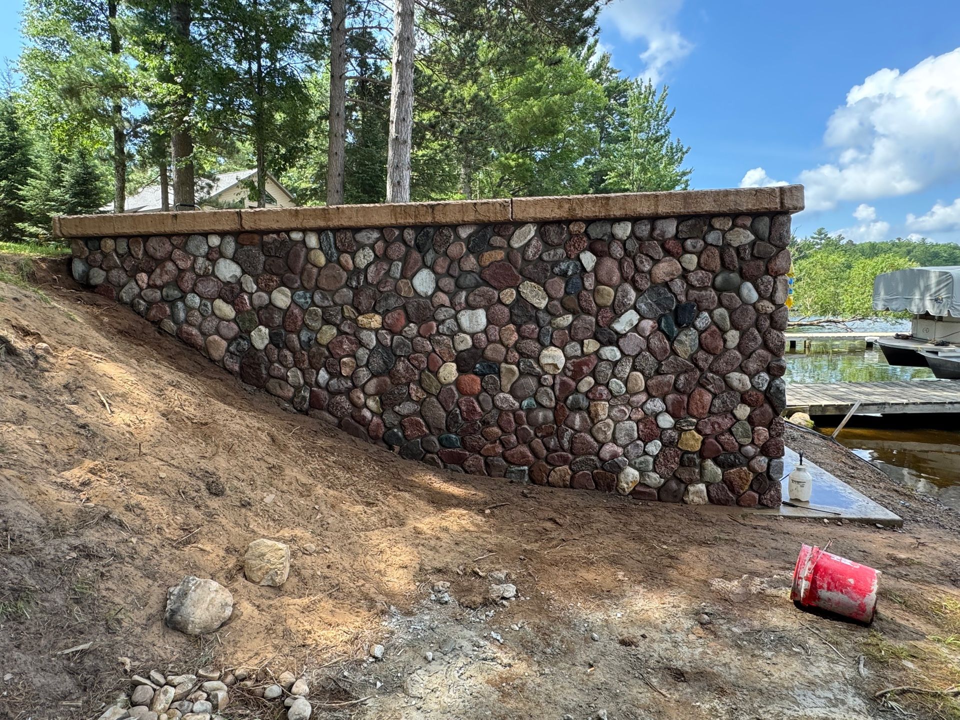 Stone retaining wall on a lake shore, with dirt slope and blue sky.