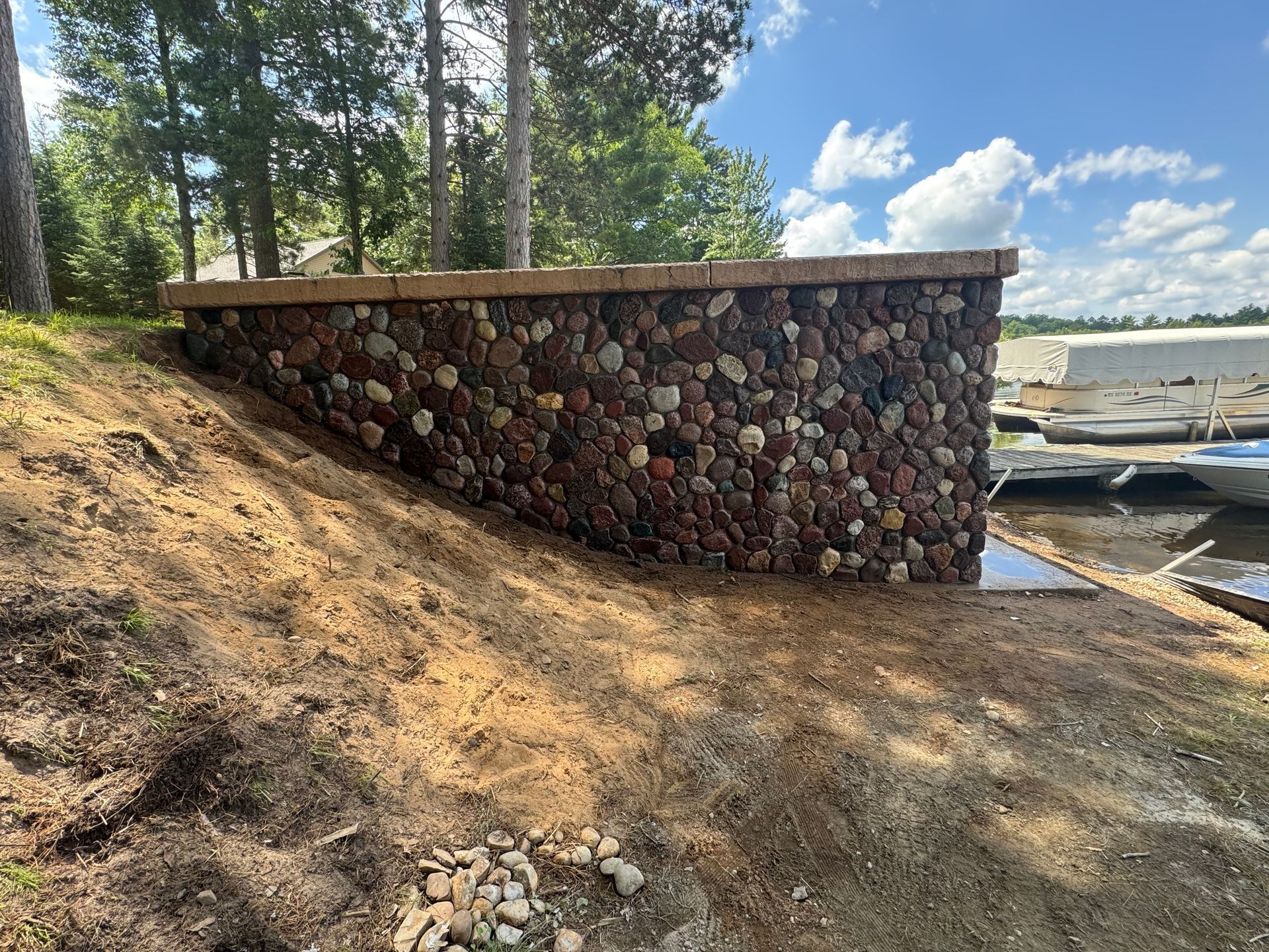 Stone retaining wall with a wooden top, situated near water and trees.