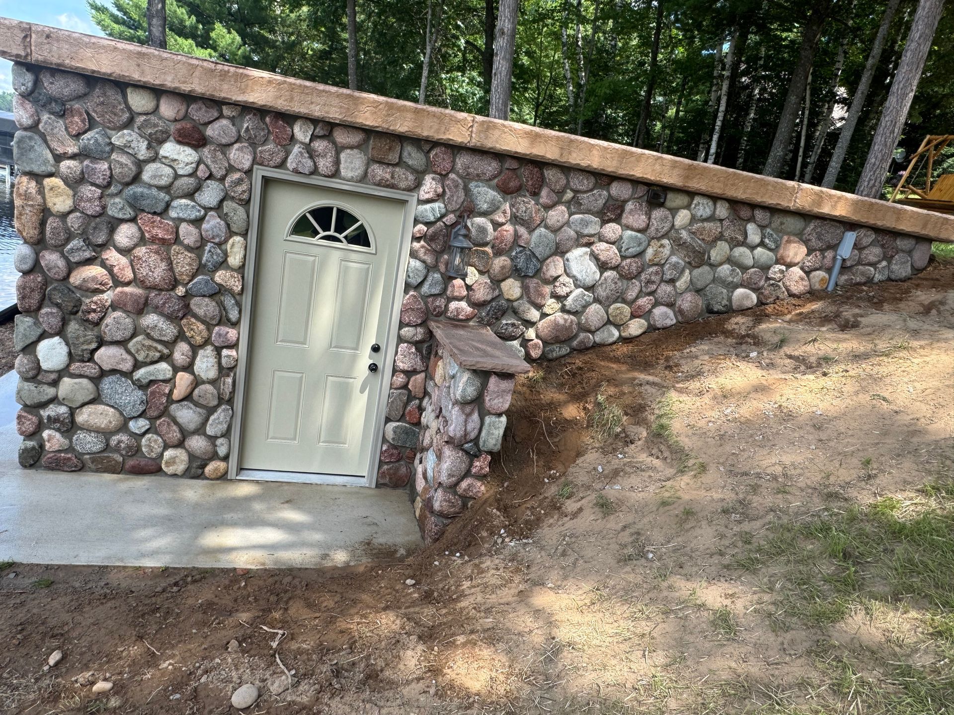 Stone-walled building with light green door and concrete entrance on a grassy slope.