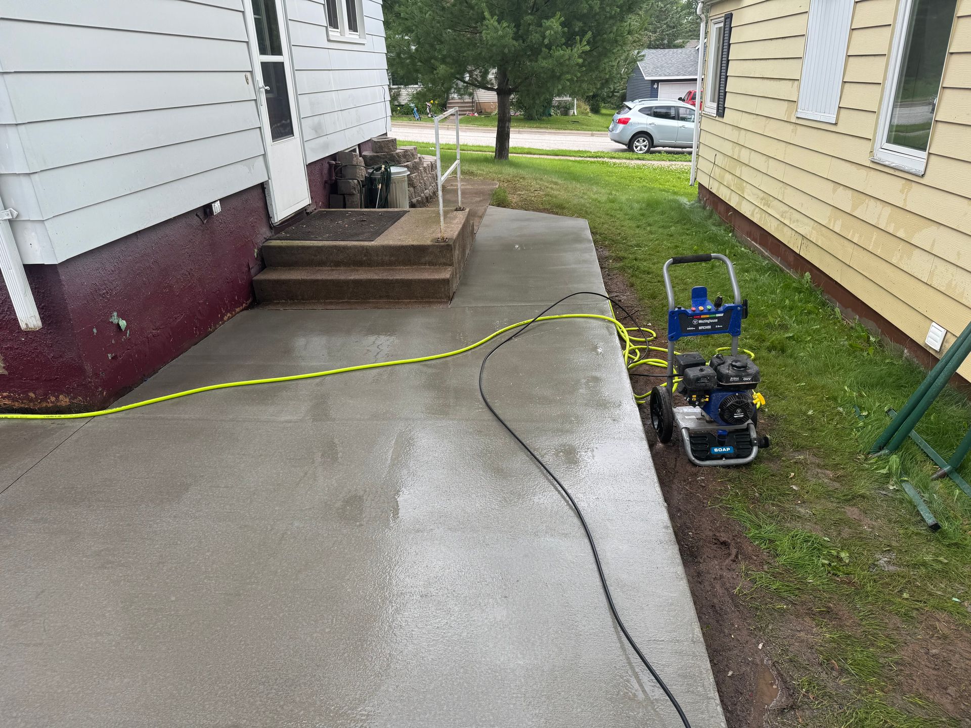 Concrete patio being cleaned with a pressure washer next to two houses.