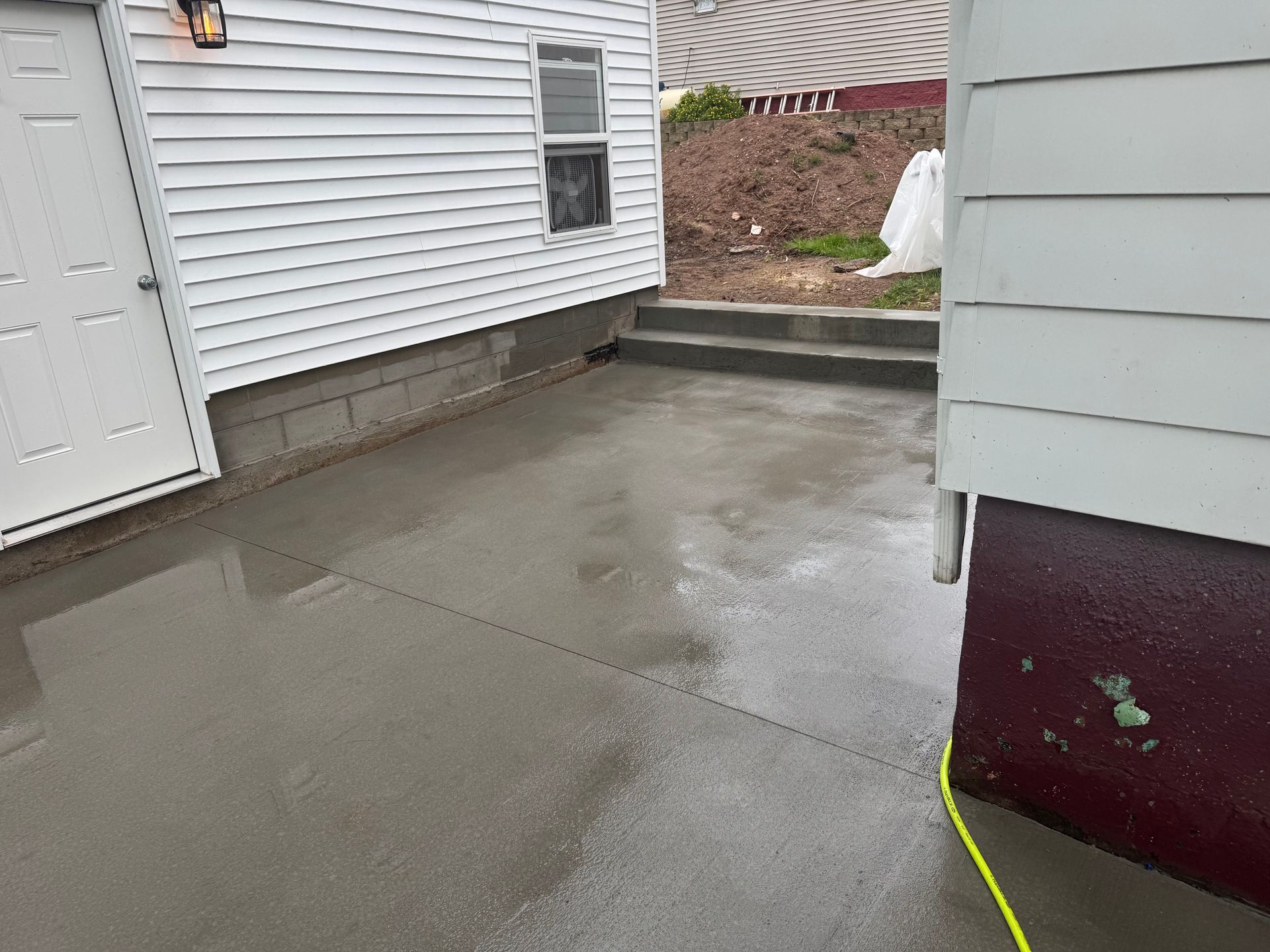 Freshly poured gray concrete patio next to a white house with a partially open door.