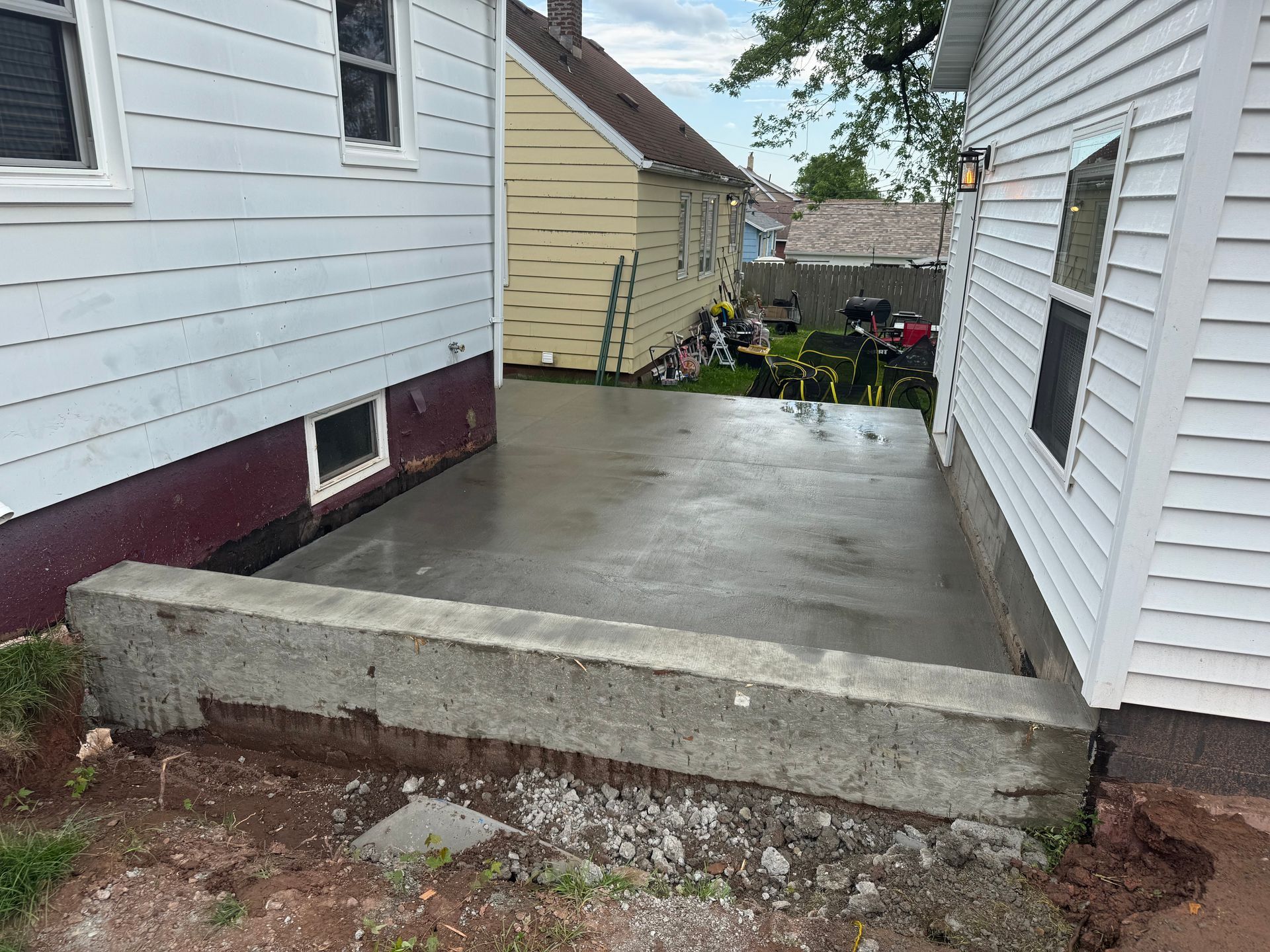 Newly poured concrete patio between two houses, with a low concrete retaining wall in front.