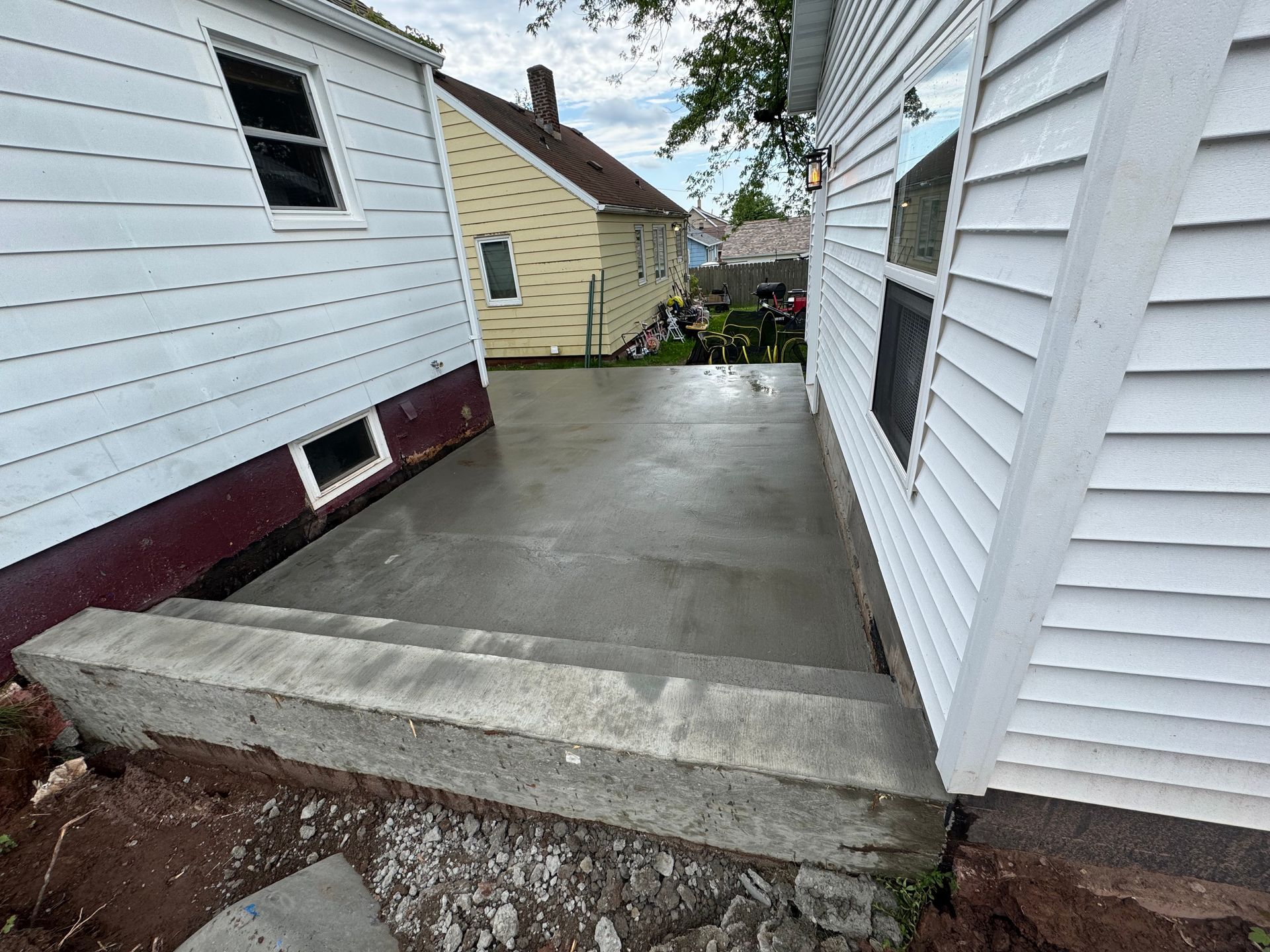 Concrete patio and steps between two white-sided houses; a sunny outdoor setting.