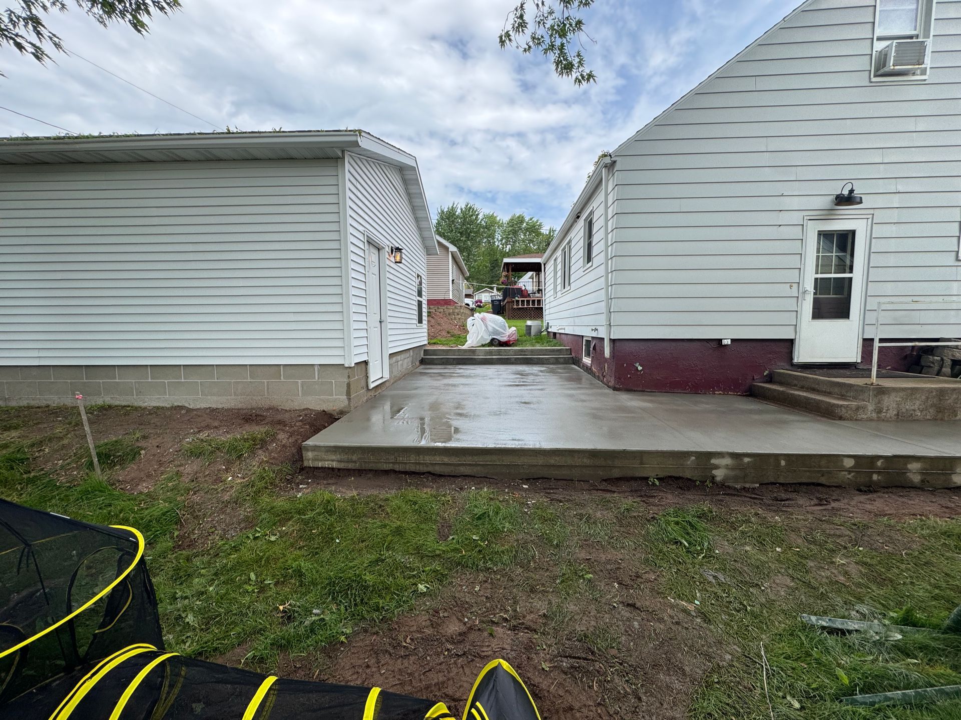 Concrete patio between two white-sided buildings. Green grass surrounds the patio.