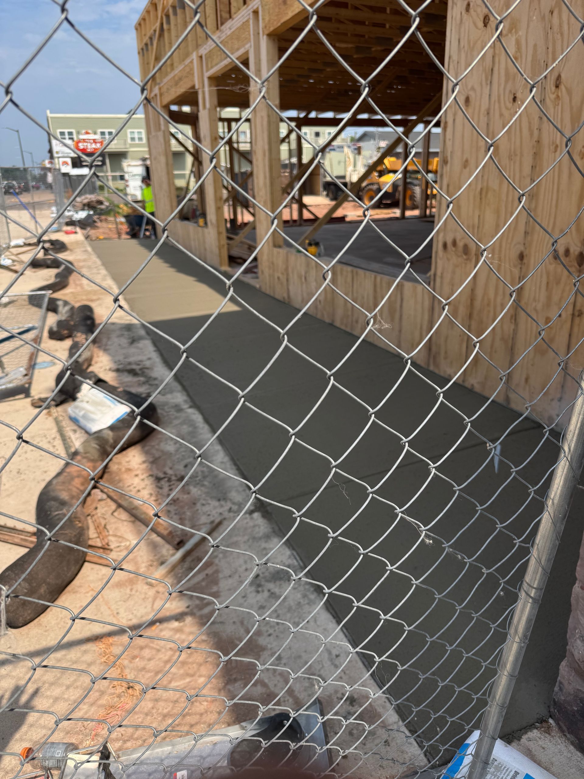 Construction site: fresh concrete walkway, wooden frame, chain-link fence.