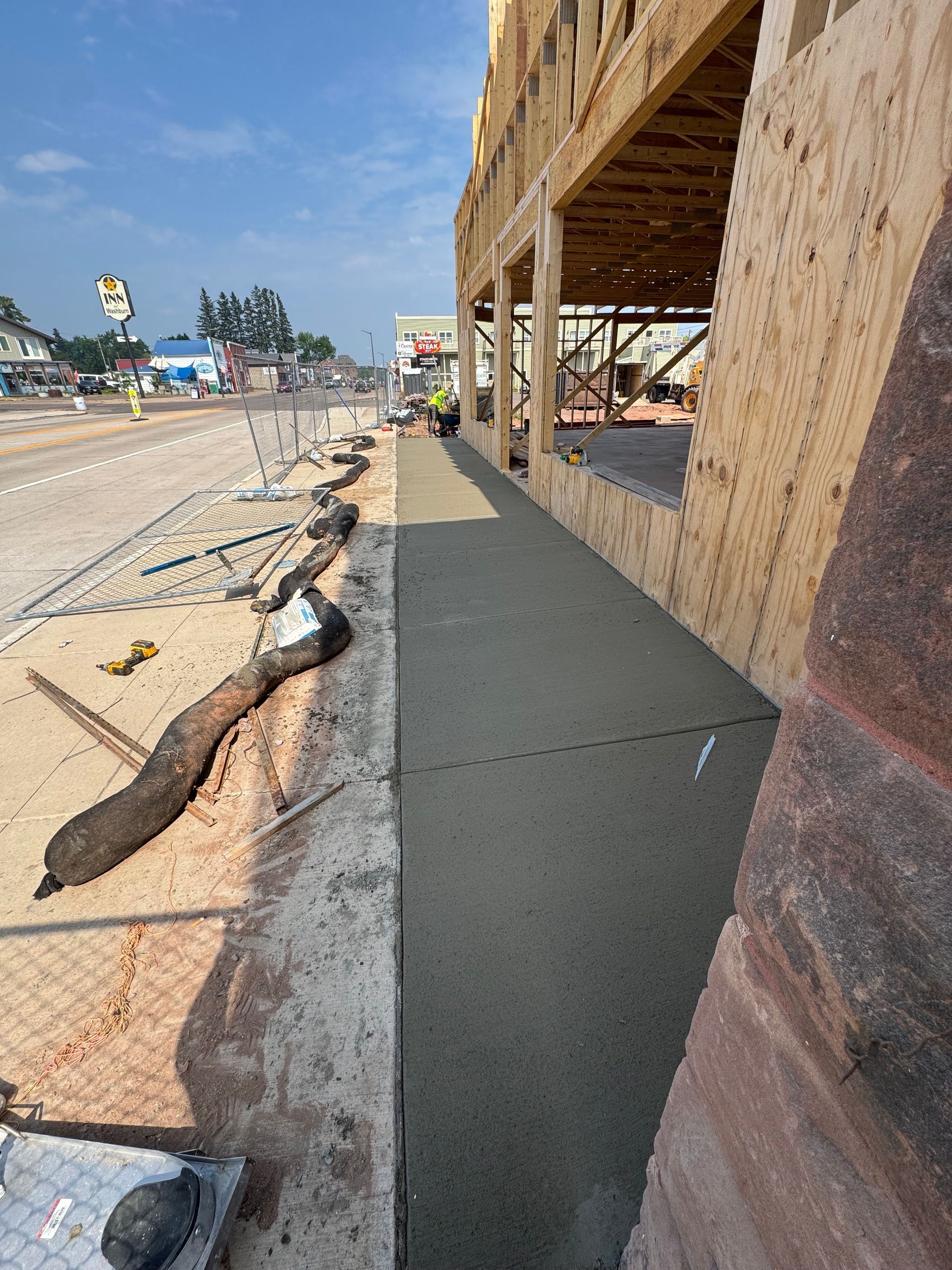 Construction site with newly poured concrete sidewalk next to a road and a building under construction.