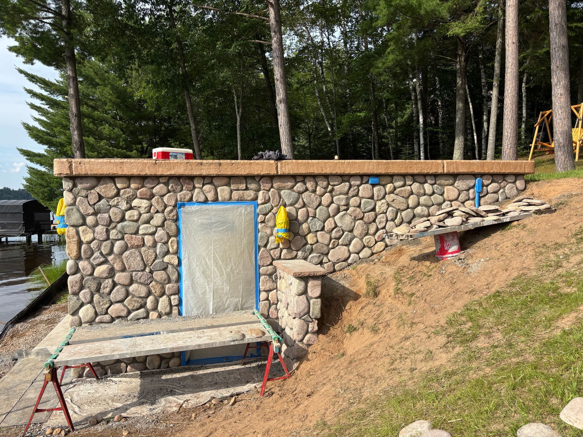 Stone structure built into a hillside, likely a boathouse. Doorway, stone exterior, and surrounding trees.