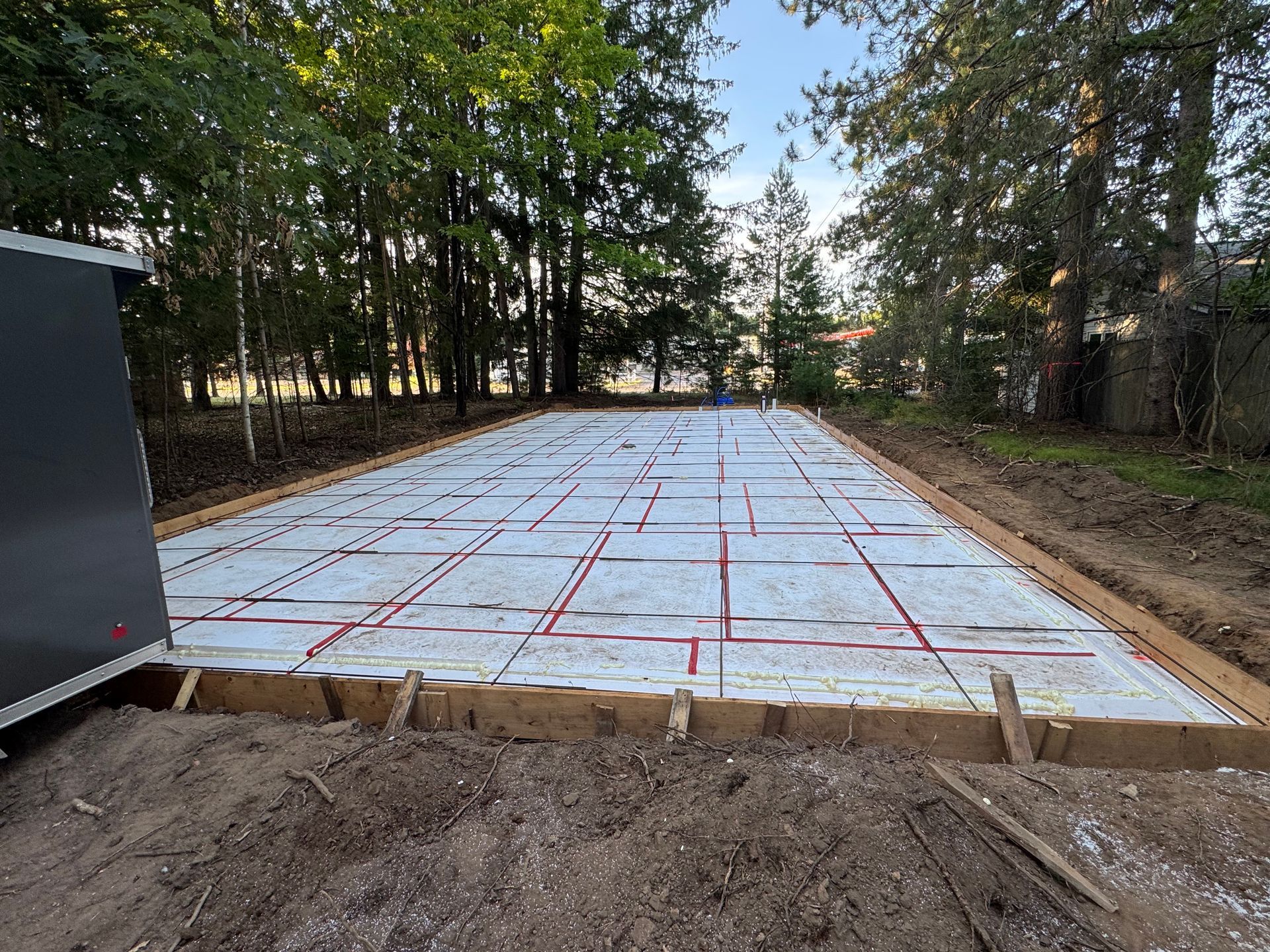 A prepared concrete foundation with wood framing, insulation, and red markings on a dirt lot.